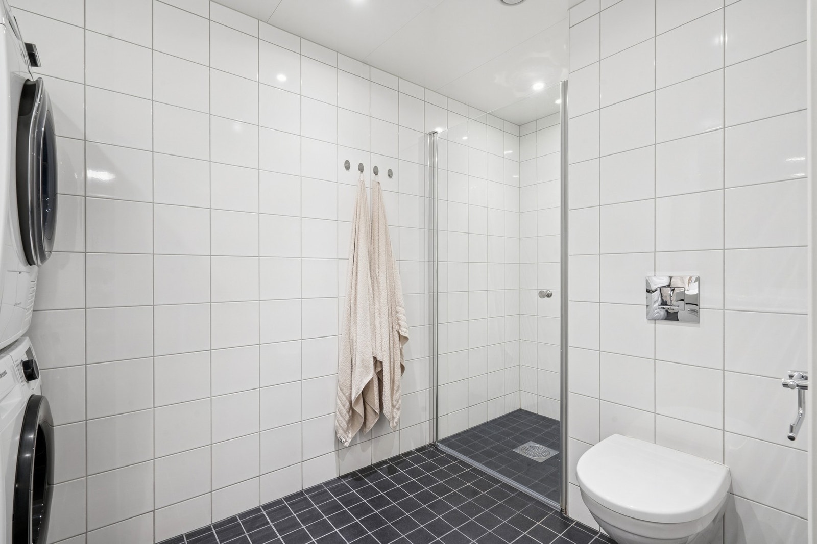 Vegghengt toalett. Dusjnisje med glassdør og ett-greps armatur med hånddusj. Opplegg for vaskemaskin/tørketrommel og 2 stikkontakter på vegg. Galleribilde