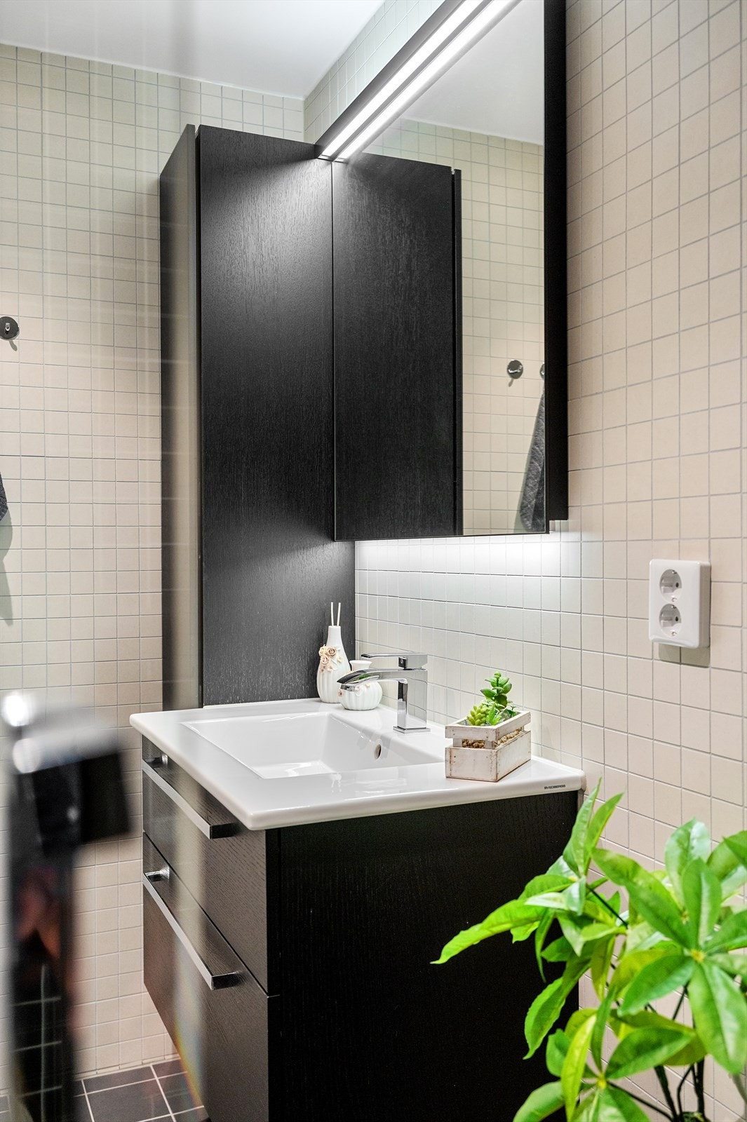 Innredningen består av vegghengt toalett, servant med innredning, speil med lys, håndklevarmer og stor dusjnisje med svingbare glassdører. Galleribilde