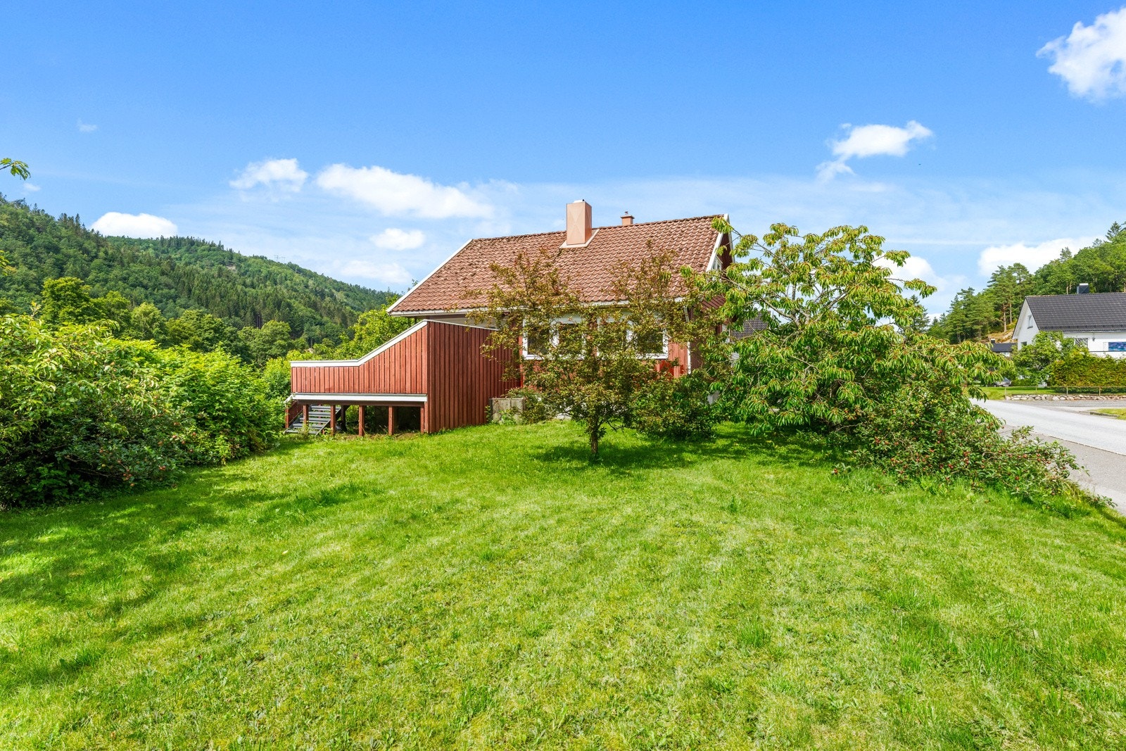 Tomten er opparbeidet med stor plen, trær, busker og annen beplatning. Galleribilde
