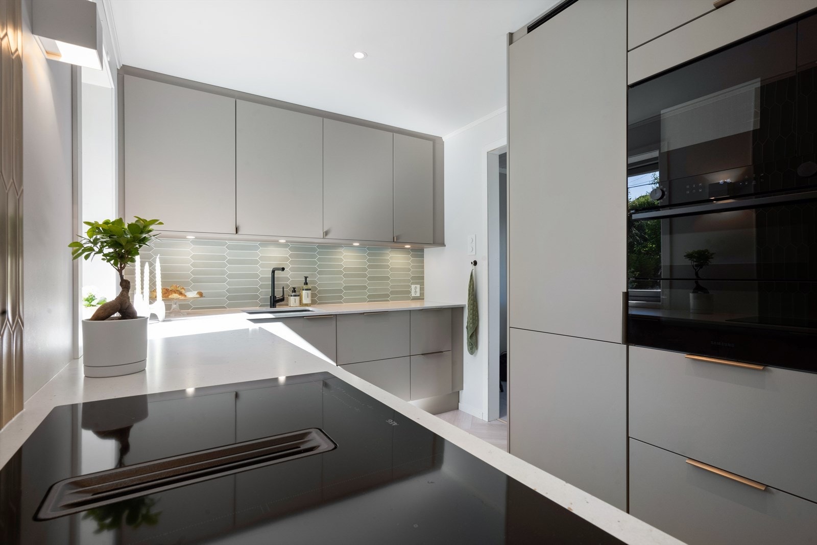 Kjøkkenet har slette fronter og benkeplate av kvartskompositt. Integrert komfyr, induksjonstopp, kjøleskap, fryseskap, mikrobølgeovn og oppvaskmaskin, alt nytt i 2024. Galleribilde