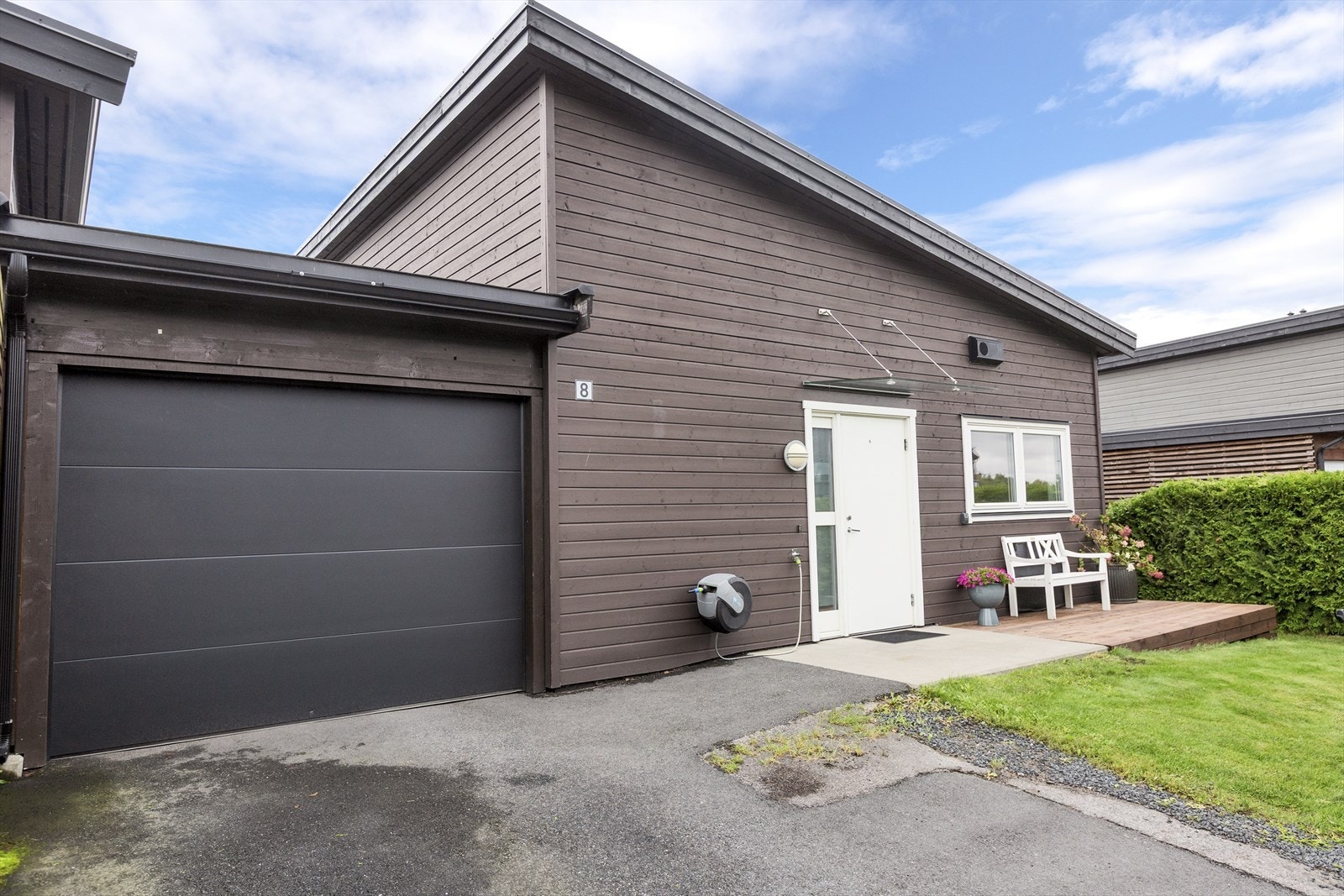 På forsiden er det liten plen, platting med morgensol, garsje med elektrisk port og billader. Plass til to bilder i asfaltert gårdsplass foran garasjen Galleribilde