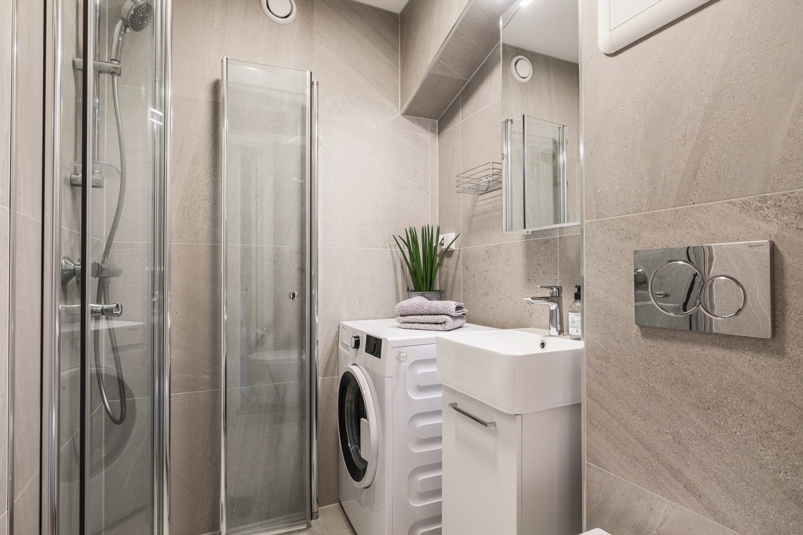 Badet er innredet med moderne fliser på vegger og gulv, som gir stilrent uttrykk. Det er opplegg for vaskemaskin. Galleribilde