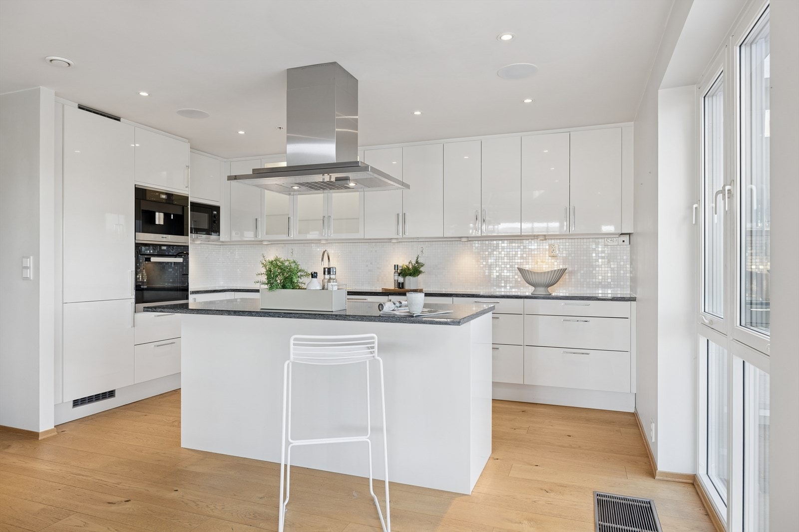 Stilrent Marbodal-kjøkken med takhøy innredning i hvite fronter, kjøkkenøy og benkeplate i stein/granitt. Galleribilde