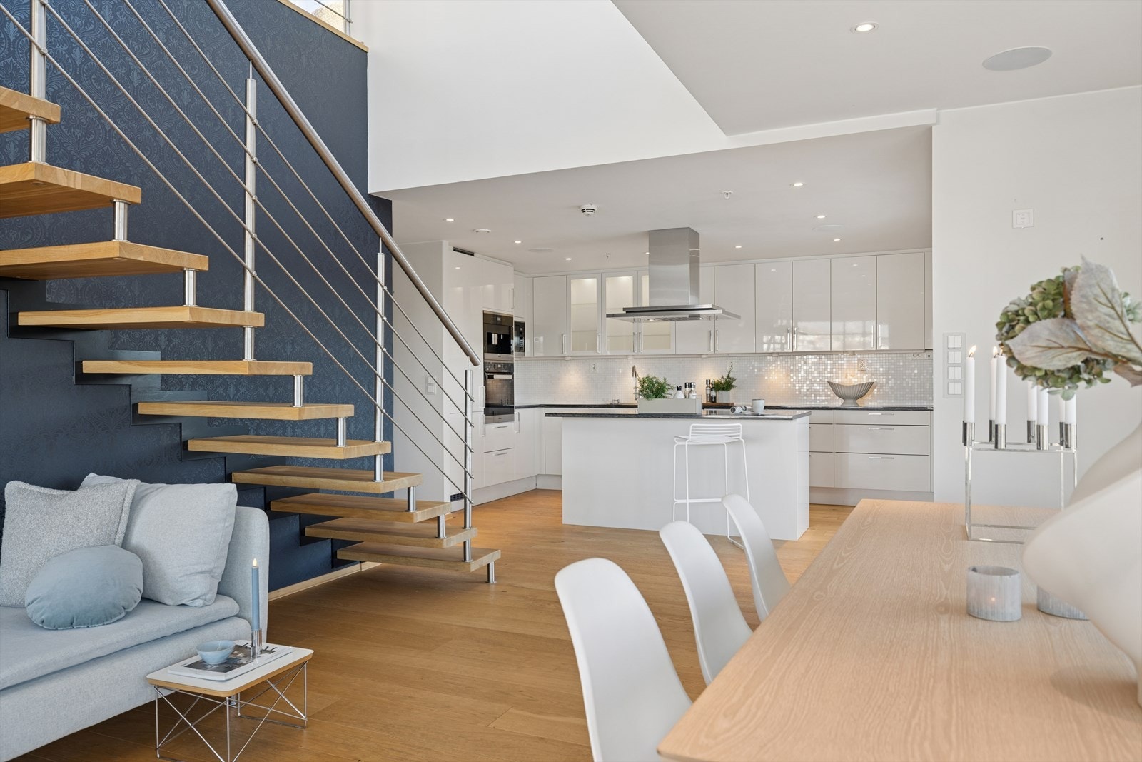 Kjøkken med delvis åpen løsning til spisestue med moderne svevende trapp med stålrekkverk til andre etasje Galleribilde