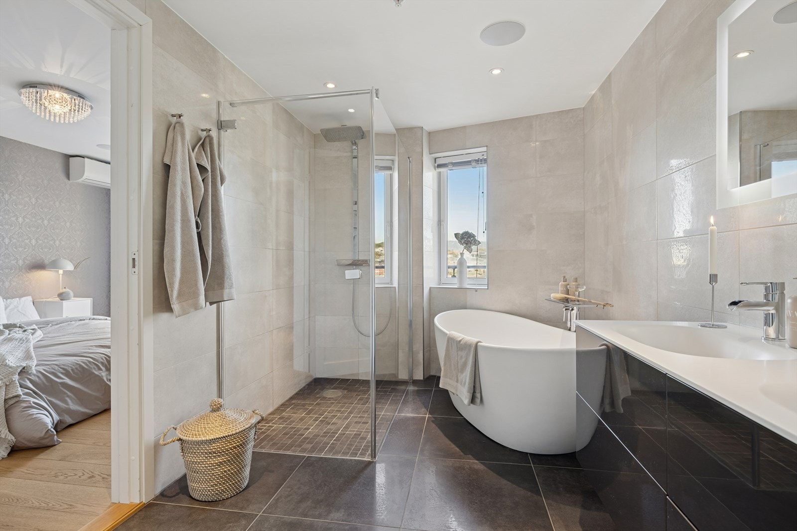 Baderom med dør fra hvoedsoverom har badekar, dusj og dobbel servant i baderomsinnredning. Speil over vask med integrert belysning Galleribilde