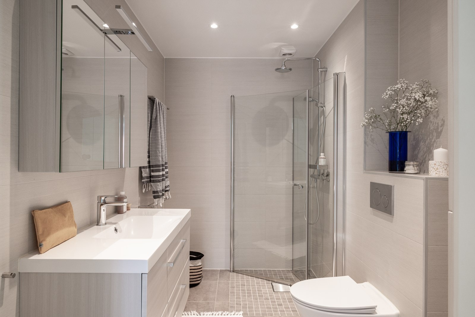 Badet i 1. etasje er stilrent, med fliser på både gulv og vegger. Dusjsonen er utstyrt med innfelte glassdører i herdet glass, som gir et åpent og ryddig uttrykk. Det er lagt varmekabler i gulvet. Galleribilde