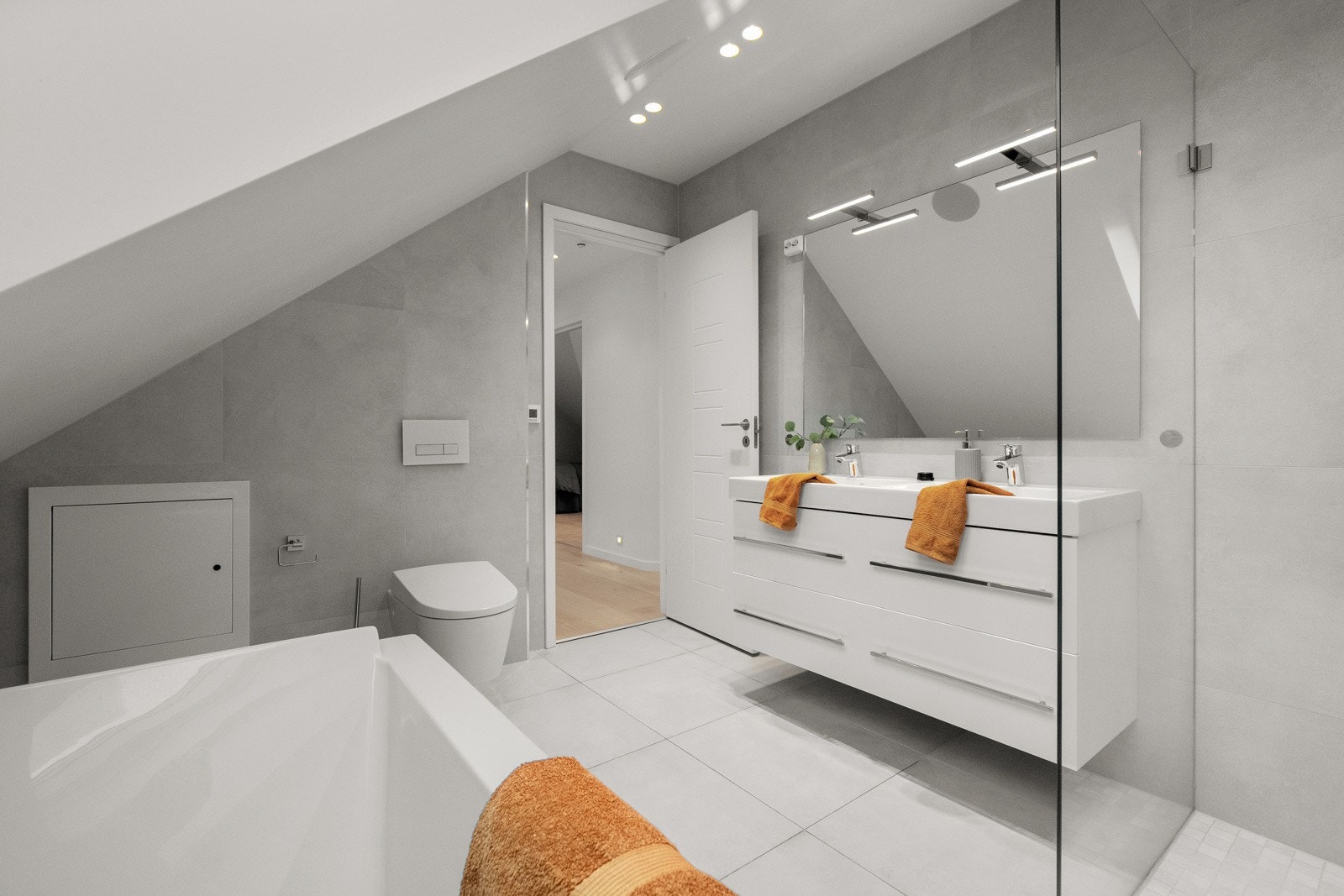 Her finner du et innmurt badekar og dusj, en veggmontert dobbel servant som gir rikelig med oppbevaringsplass