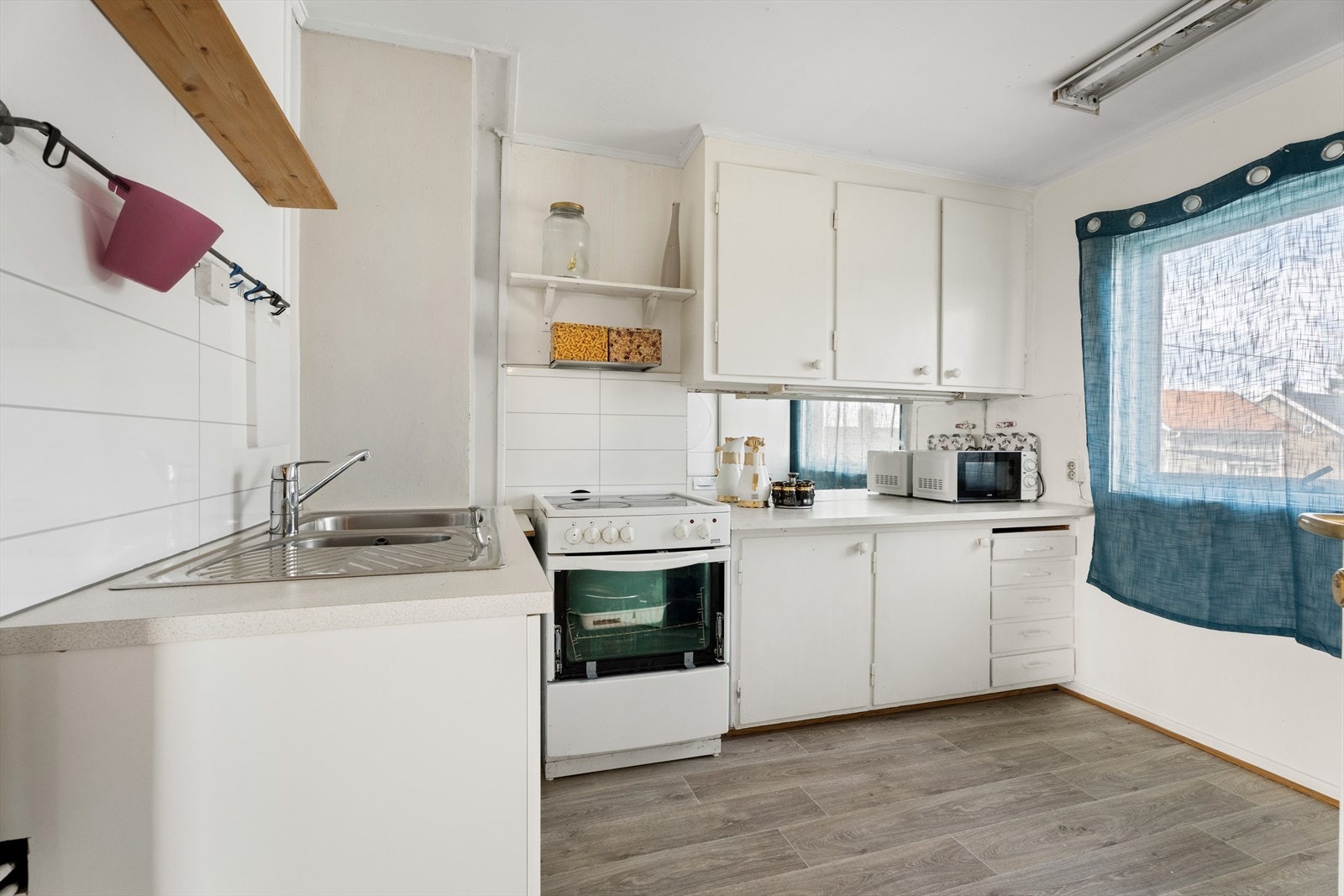 Kjøkkenet har eldre innredning med lyse, slette fronter, laminert benkeplate og nedfelt oppvaskkum Galleribilde