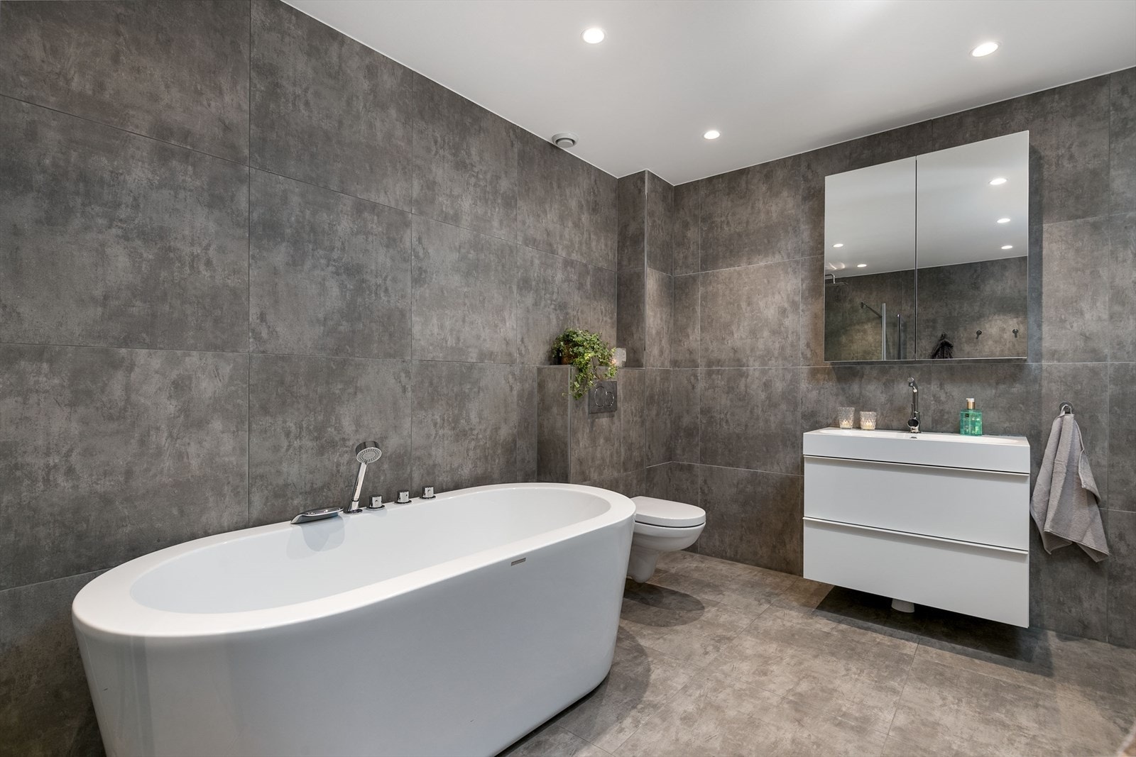 Planløsningen er praktisk, med toalett i alle etasjer. Nede er badet av god størrelse, innredet med store vegg- og gulvfliser i ulike gråtoner. Galleribilde