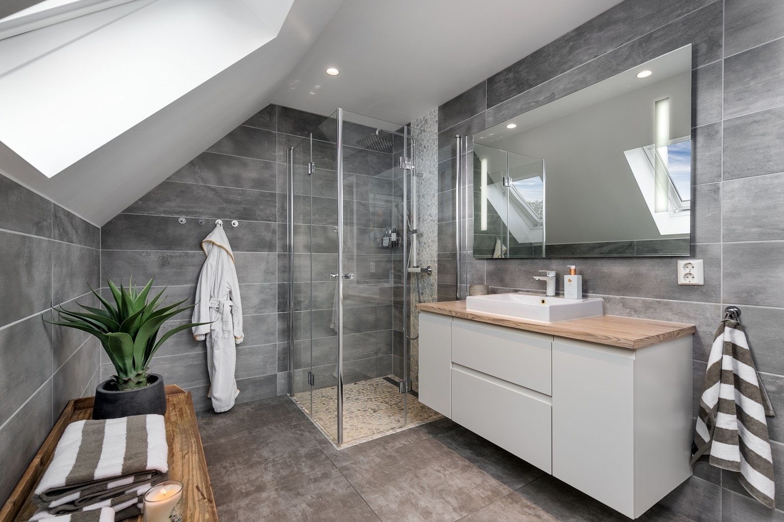 Et dusjhjørne er utstyrt med rullestein, slukrenne, regnfallsdusj og innfellbare glassdører. Baderomsinnredningen består av et stort speil og en hvit skapseksjon med toppmontert servant. Galleribilde