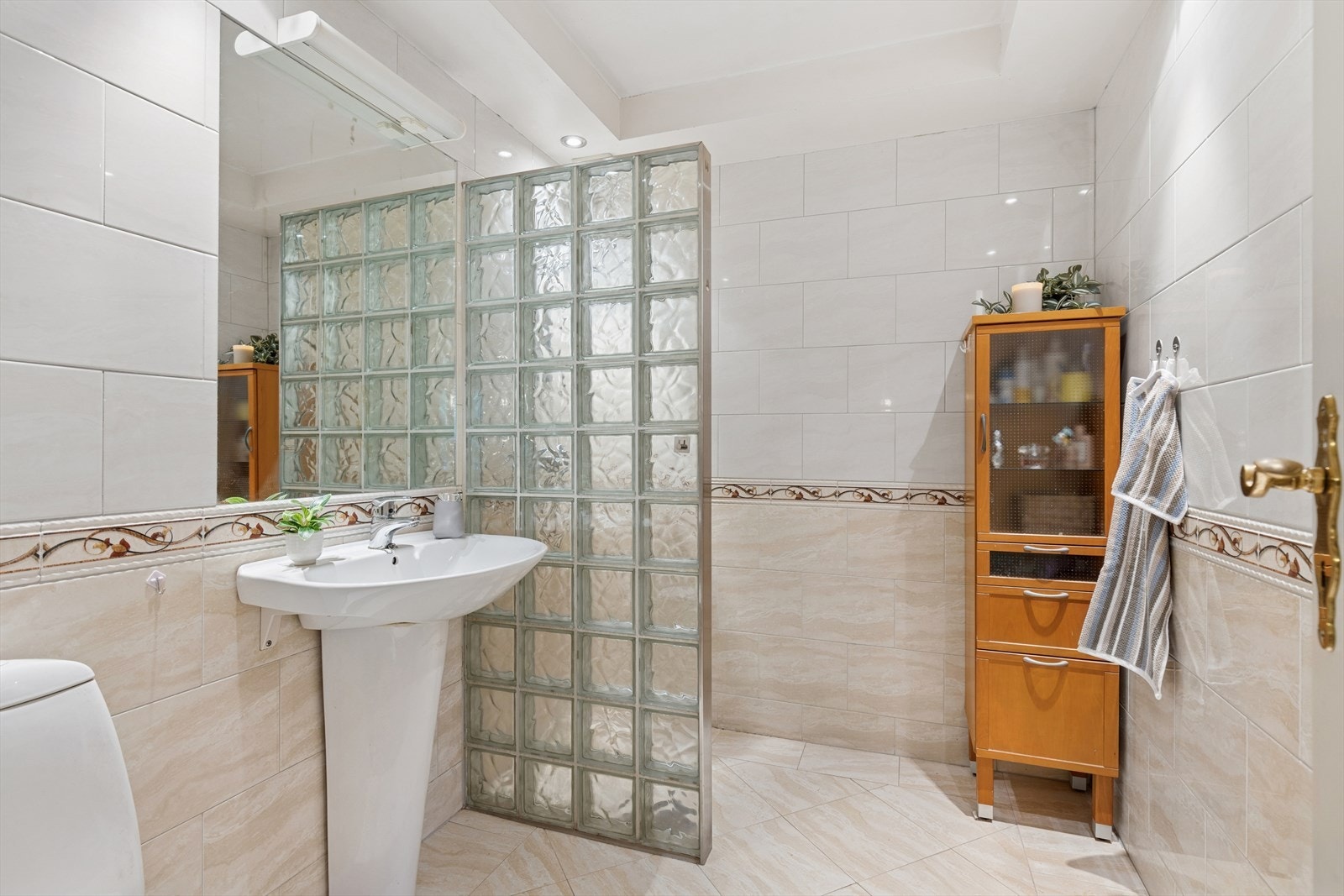 Pent bad med flislagte vegg- og gulvflater, varmekabler på gulv, himling med slette overflater og downlights. Galleribilde