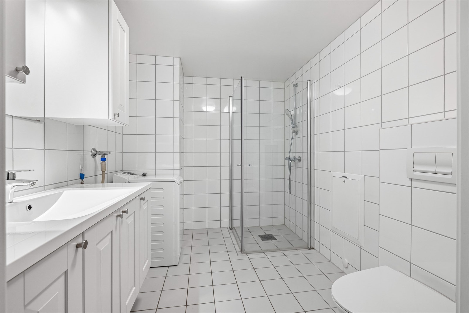 Flislagt bad med varme i gulv, vegghengt toalett og opplegg til vaskemaskin. Innfellbare dusjdører i glass Galleribilde