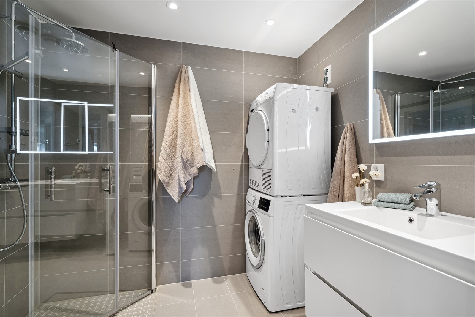 Det vakre badet er lekkert innredet med en hvit servantinnredning, speil med integrerte lys, toalett og dusjhjørne med glassdører og regnfallsdusj. Du har også opplegg for vaskemaskin og plass til tørketrommel. Galleribilde