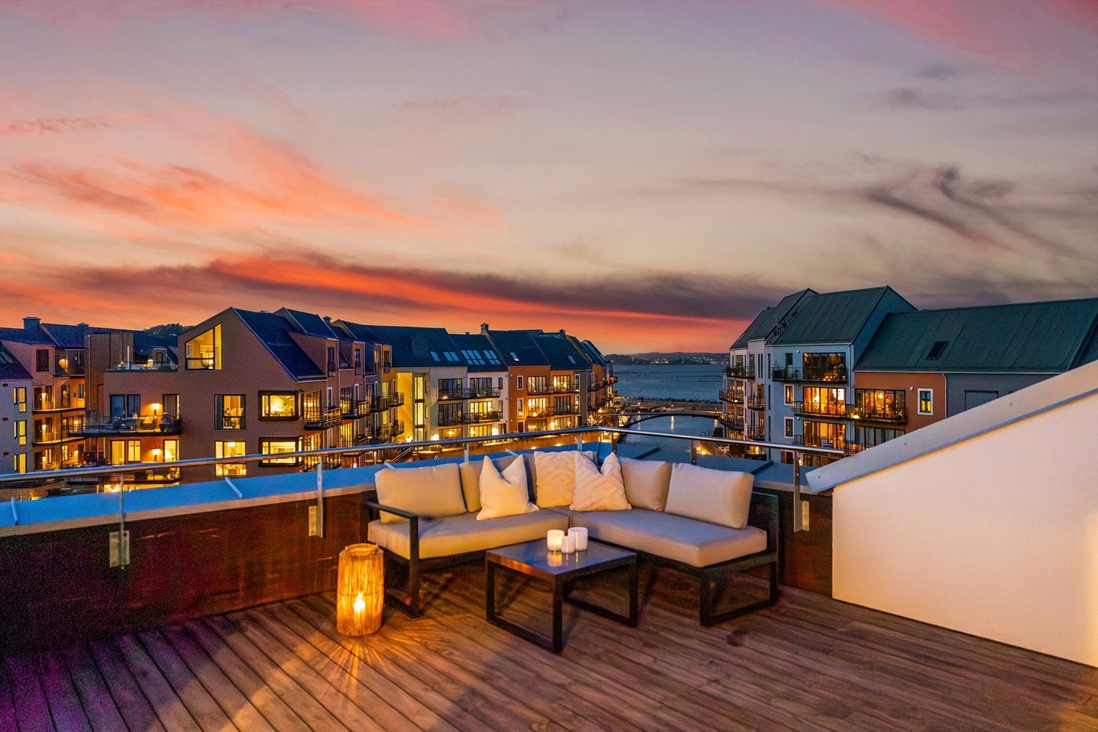 Stemningsfull takterrasse med vakker utsikt mot sjøen og moderne leilighetsbygg, perfekt for avslapning ved solnedgang. Galleribilde