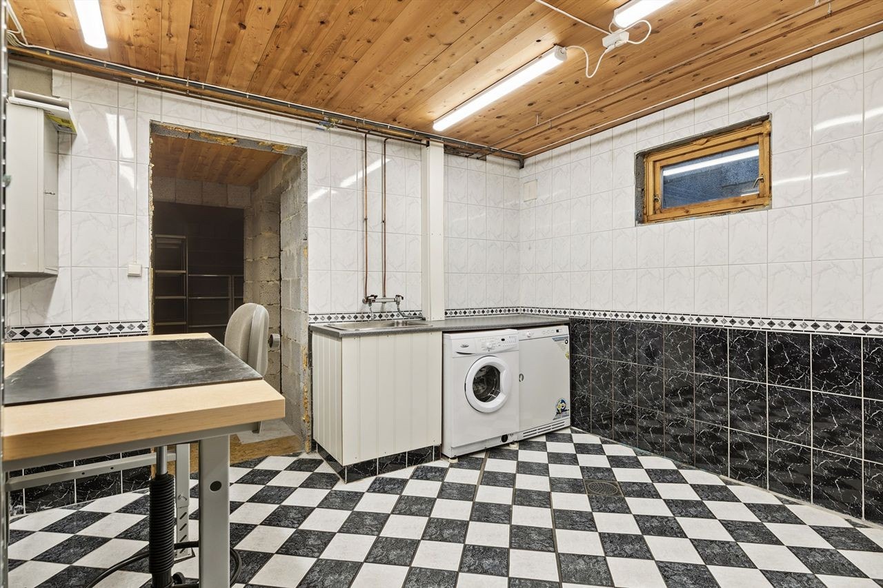 Romslig, flislagt vaskerom i kjelleren med arbeidsbenk og nedfelt vaskekum. Galleribilde