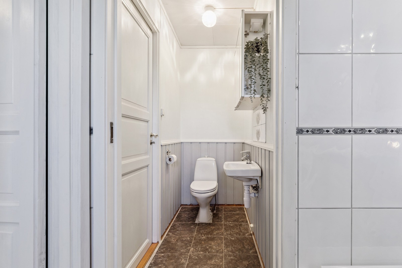 Toalettrom med flislagt gulv, brystningspanel og speilskap. Galleribilde