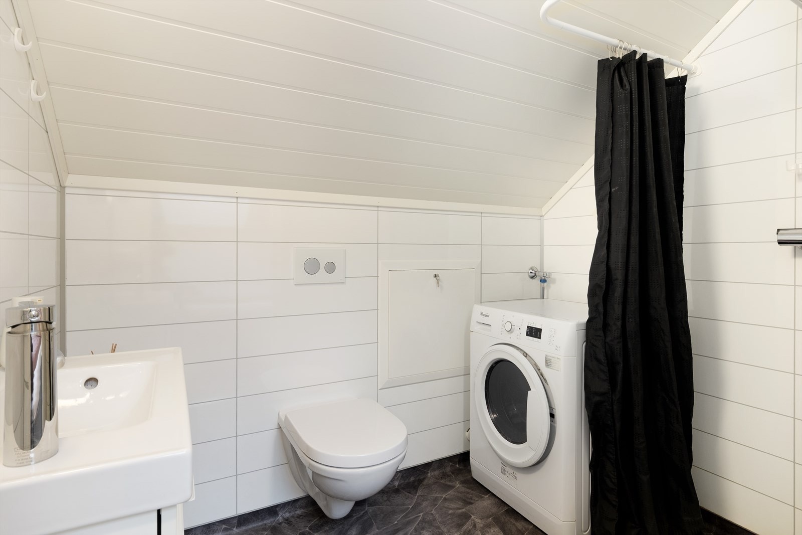 Badet inneheld vegghengt toalett, nedfelt servant med underksåp, opplegg for vaskemaskin og dusjhjørne med forheng. Galleribilde