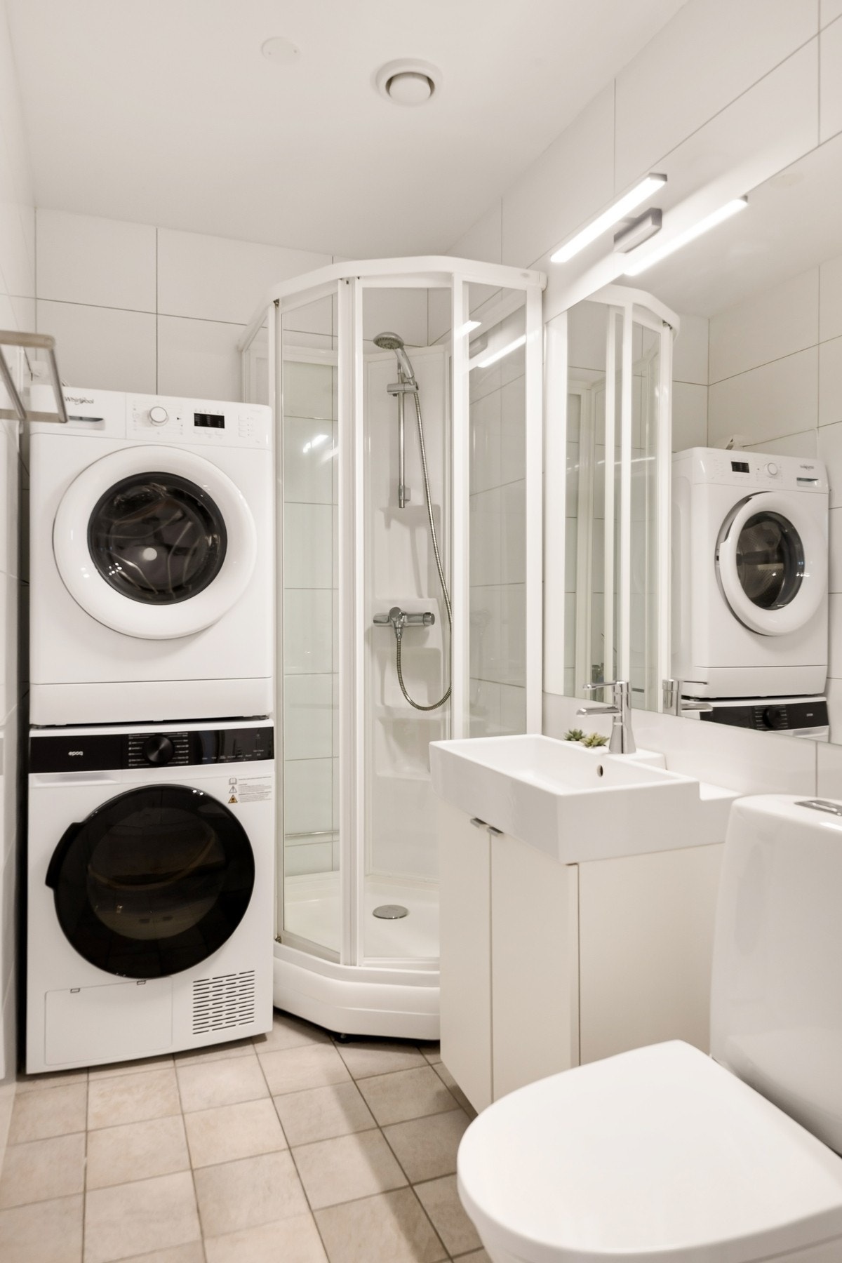 Flislagt bad med varmekabler i gulv. Badet er utstyrt med dusjkabinett, opplegg for vaskemaskin, baderomsinnredning og gulvstående wc Galleribilde