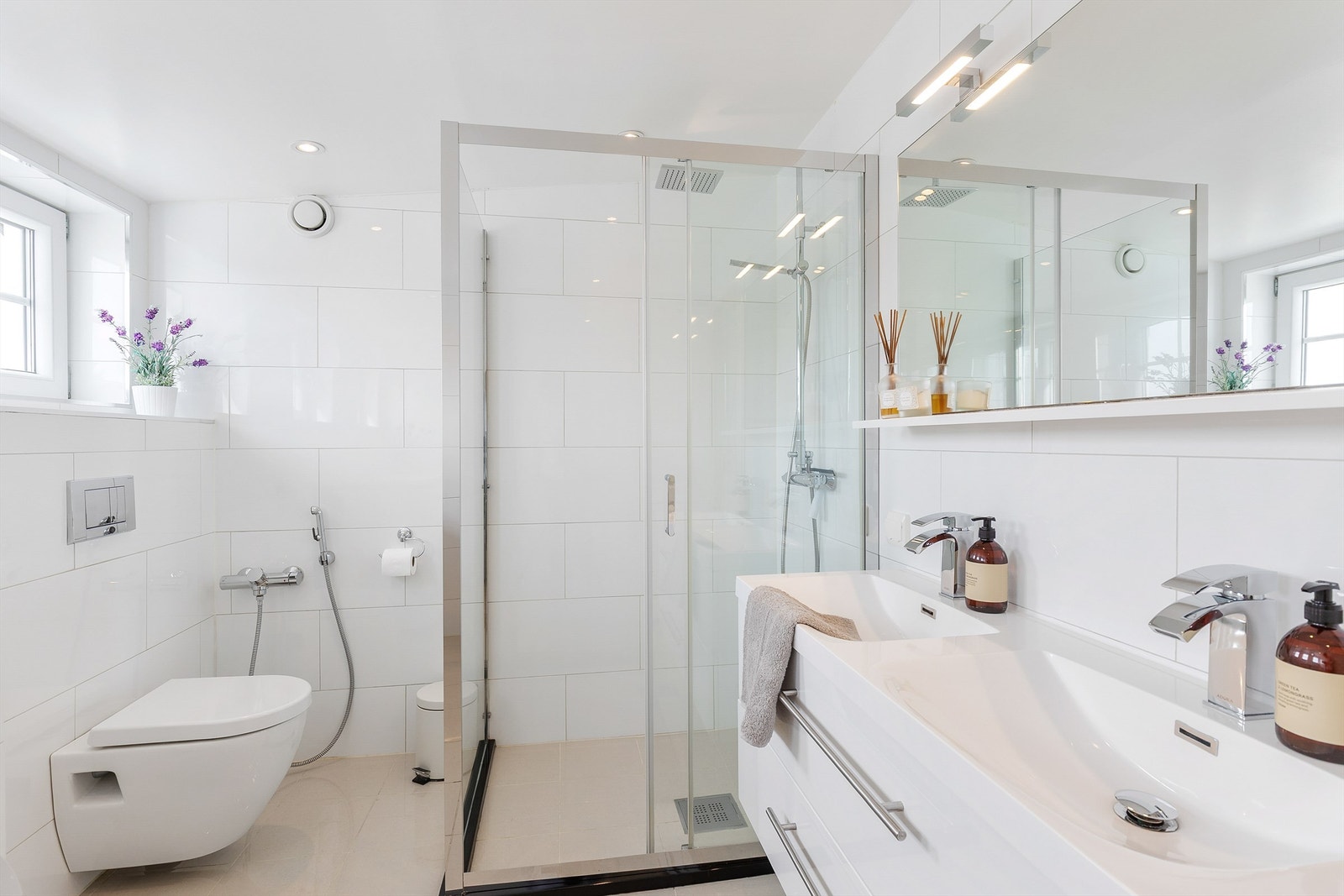 Boligens andre bad er pent flislagt på gulv og vegger med elektrisk gulvvarme. Badet er innredet med vegghengt klosett, dobbel servant nedfelt i innredning, speil med belysning og dusjhjørne med glassdører. Galleribilde