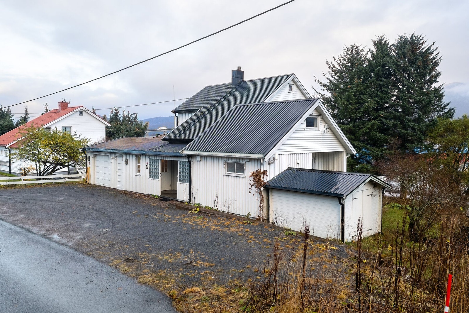 Gruslagt innkjørsel og gårdsplass med plass til parkering for flere biler, i tillegg til garasjen. Til høyre er uteboden. Galleribilde