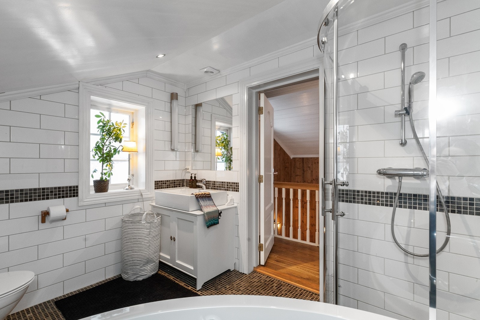 Badet har hvite fliser på vegg og sort mosaikk på gulv Galleribilde