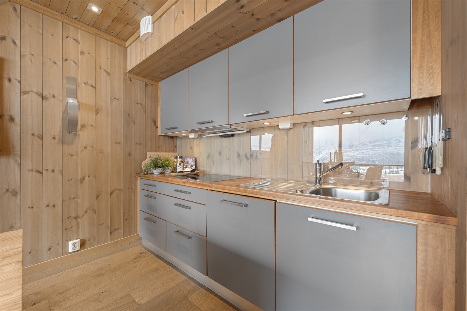 Kjøkkeninnredning fra Smedstorp er lekker i moderne utførelse med grå glatte fronter og benkeplate i eik. Oppvaskkum med ettgreps blandebatteri. Integrert kaffemaskin, oppvaskmaskin, stekeovn, kjøl og fryseskap, samt steketopp og ventilator. Galleribilde