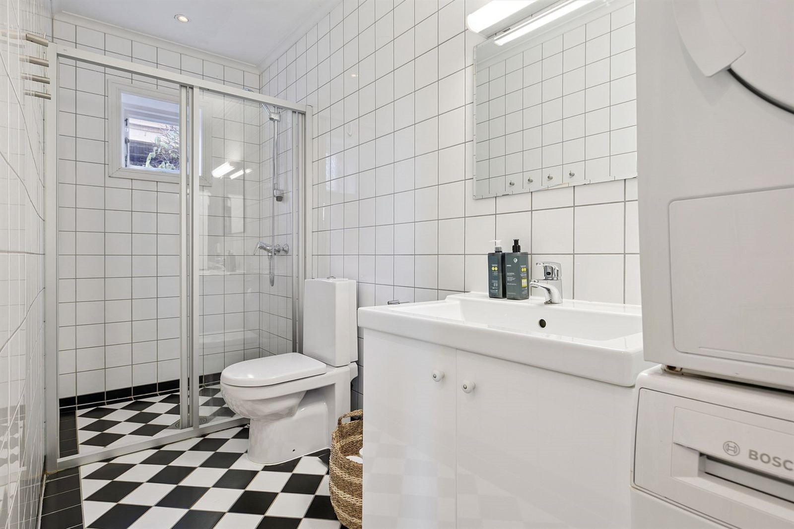 Stilig bad med et praktisk dusjhjørne, servant med doble skapdører og medfølgende vaskemaskin og tørketrommel Galleribilde