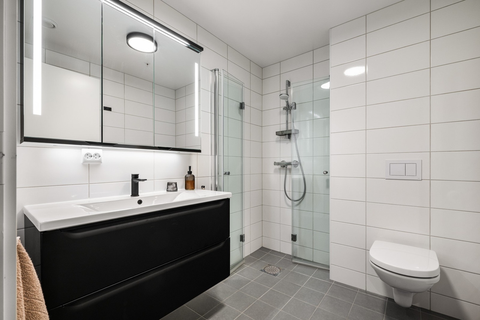 Rommet inneholder vegghengt toalett, helstøpt servant, skuffer under servant med slette fronter, dusjdører i klart glass. Galleribilde