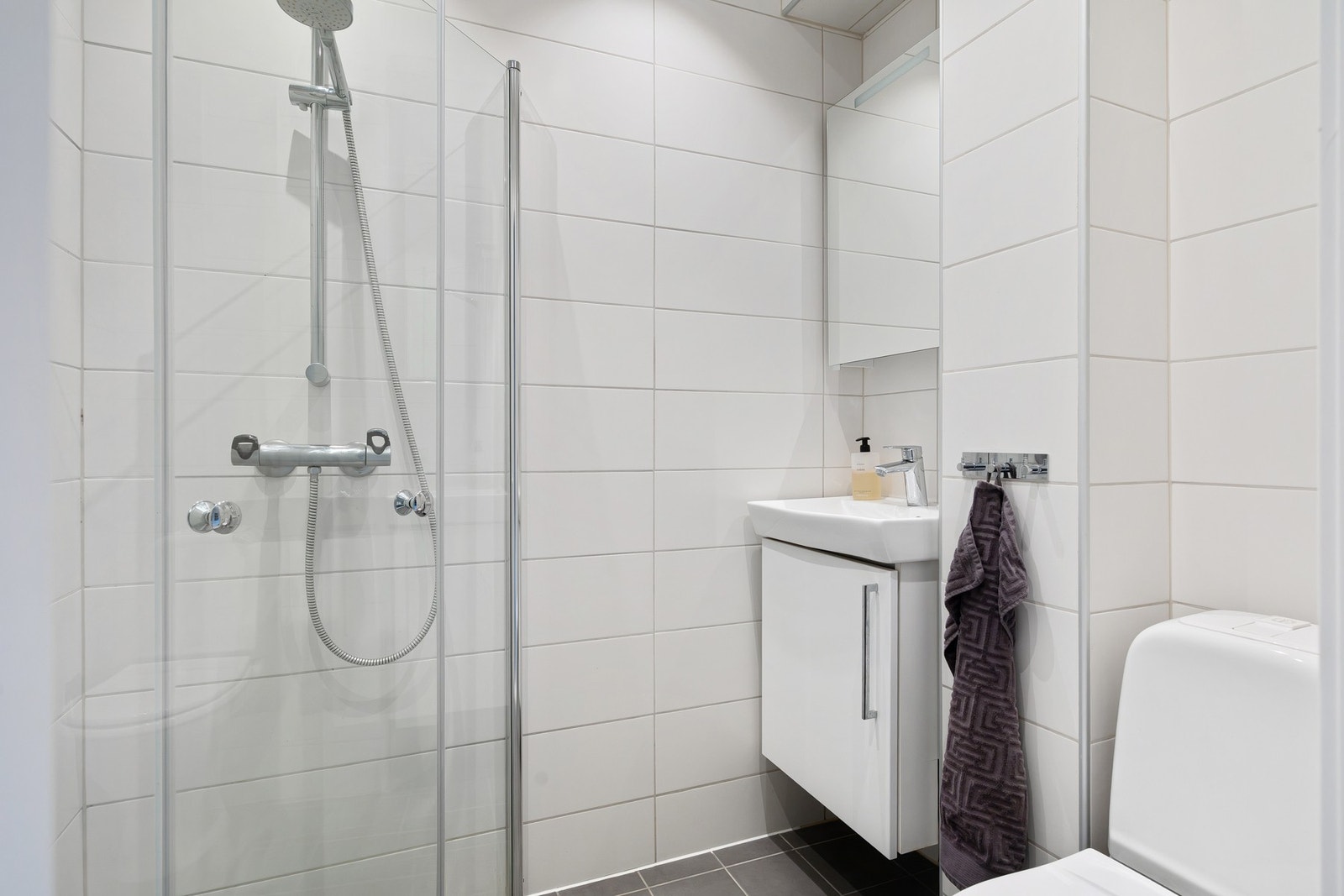 Badet er innredet med servantskap med nedfelt servant, veggskap med speil, gulvmontert toalett og dusjhjørne. Galleribilde