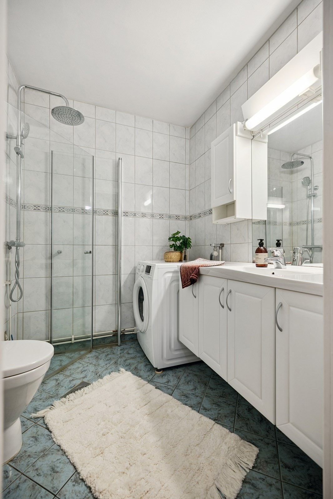 Badet er flislagt og utstyrt med dusjhjørne, servantinnredning og opplegg for vaskemaskin. Galleribilde