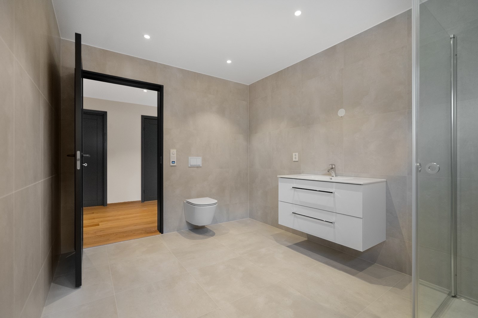 Romslig og stilrent bad med moderne innredning, vegghengt toalett og store fliser som gir et eksklusivt preg Galleribilde