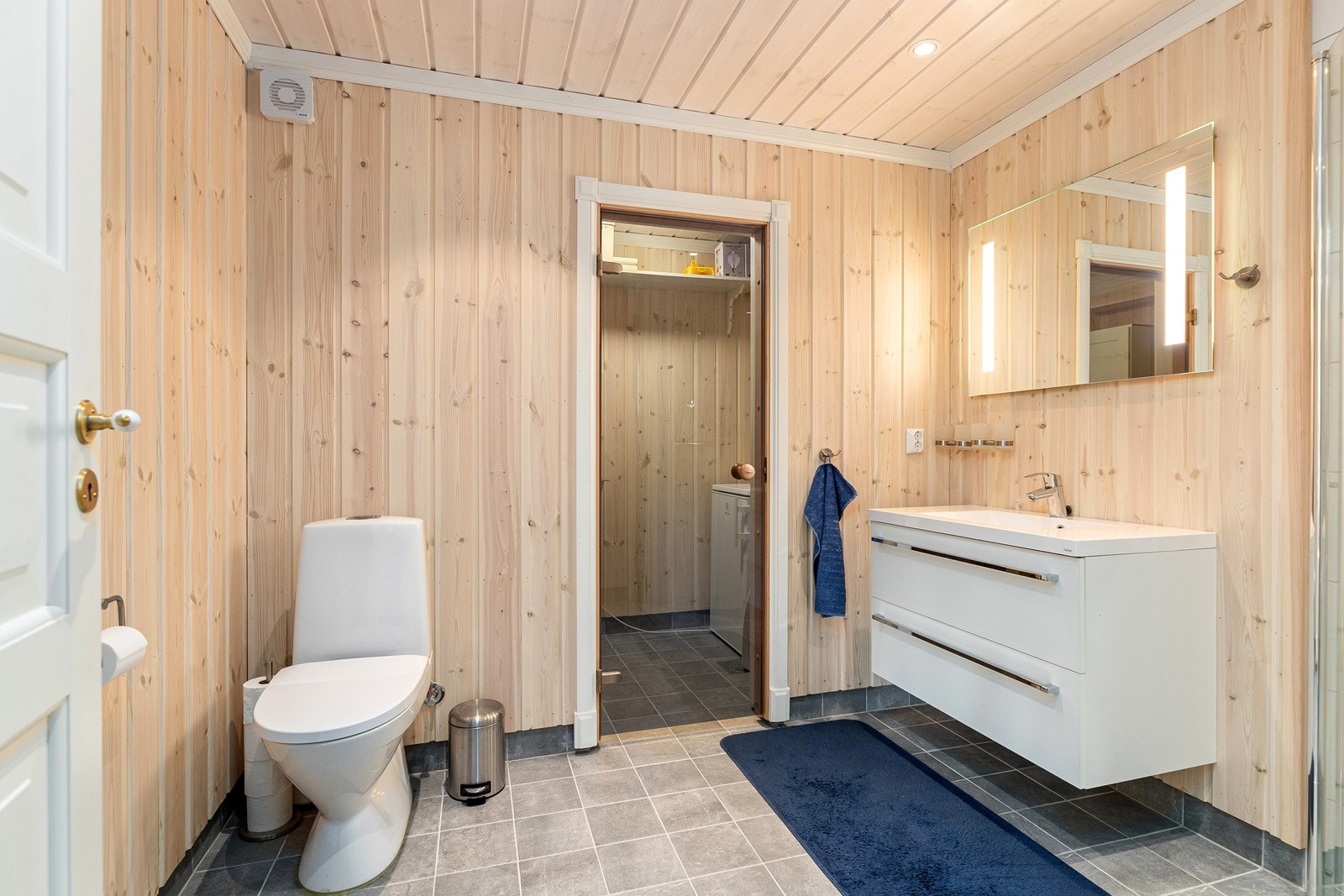 Badet i 1.etasje med flislagt gulv, innredet med servant med skuffer, dusj med glassvegger og gulvmontert toalett. Her har man videre adkomst til vaskerom. Galleribilde