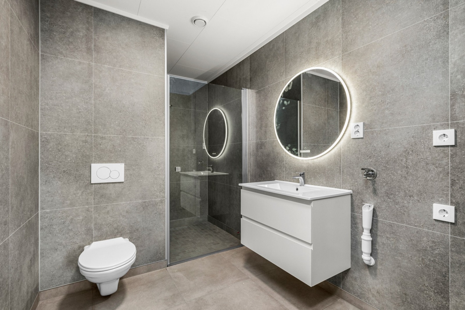 Badet har innredning med nedfelt servant, veggmontert toalett, dusjkabinett og opplegg for vaskemaskin Galleribilde