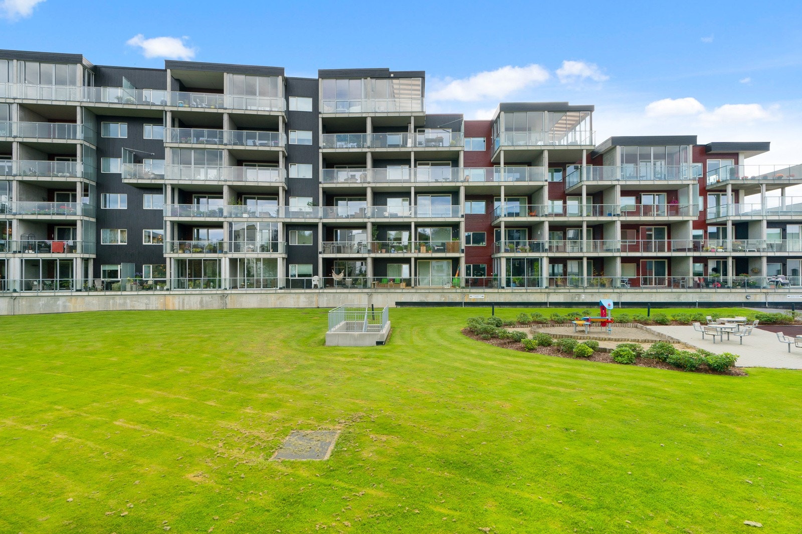 Boligens fellesarealer er godt tilrettelagt med grønne plener og flere sittebenker, noe som skaper et hyggelig og brukervennlig uteområde. Galleribilde