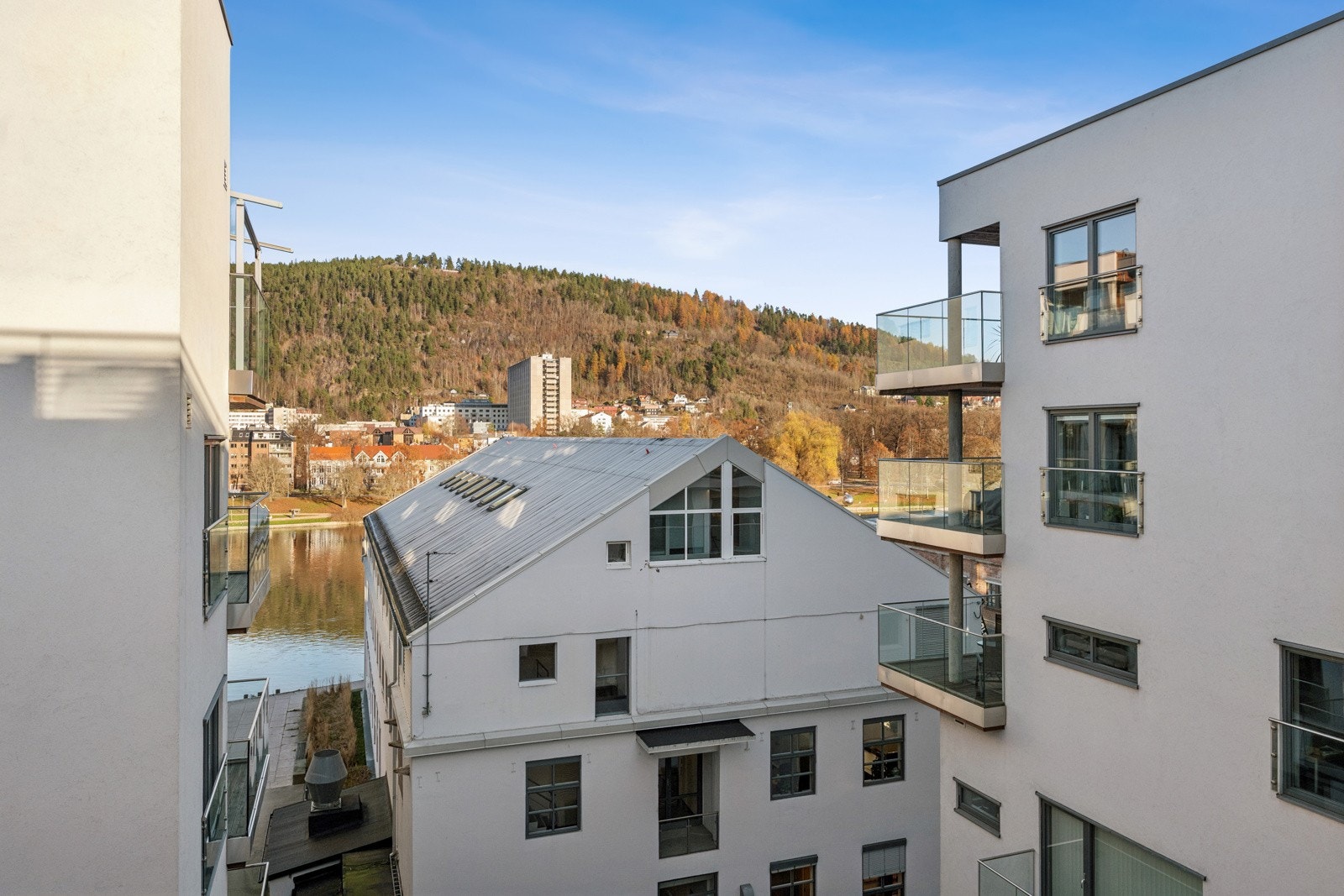 Fin utsikt mellom byggene med glimt av elven og åsen i bakgrunnen. Galleribilde
