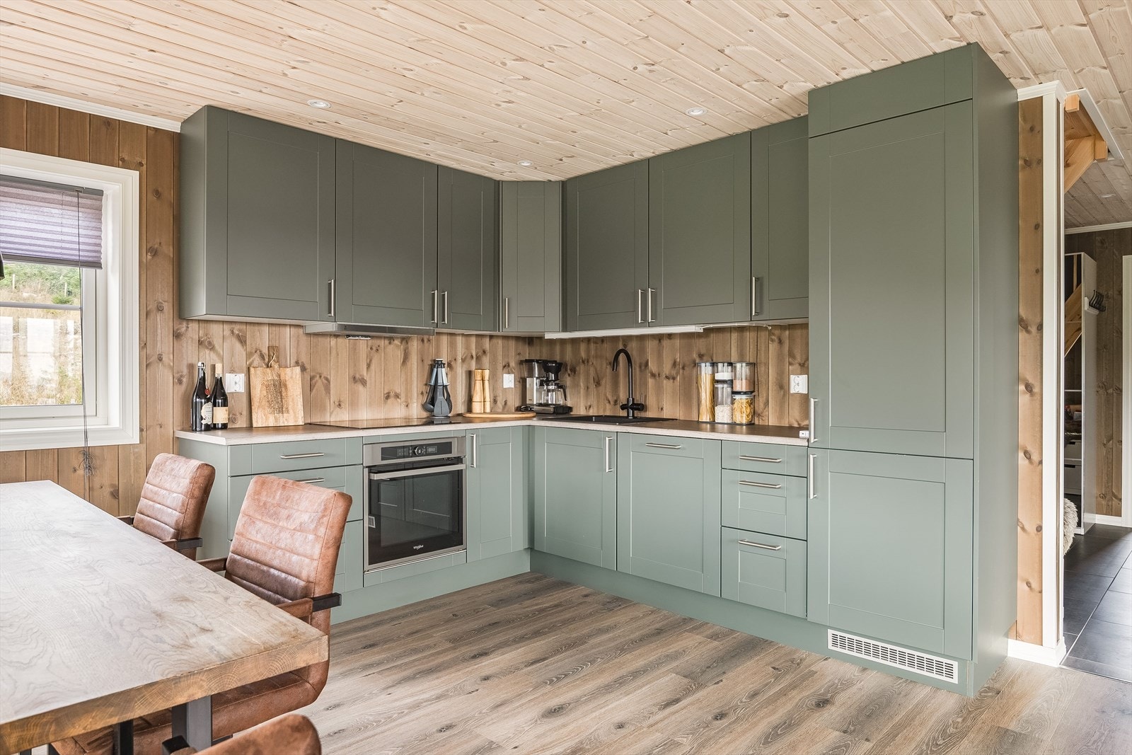 Innredningen har profilerte fronter i en nydelig grønnfarge og laminert benkeplate med nedfelt oppvaskkum. Praktisk med takhøye overskap med belysning under og downlights i himlingen. Galleribilde