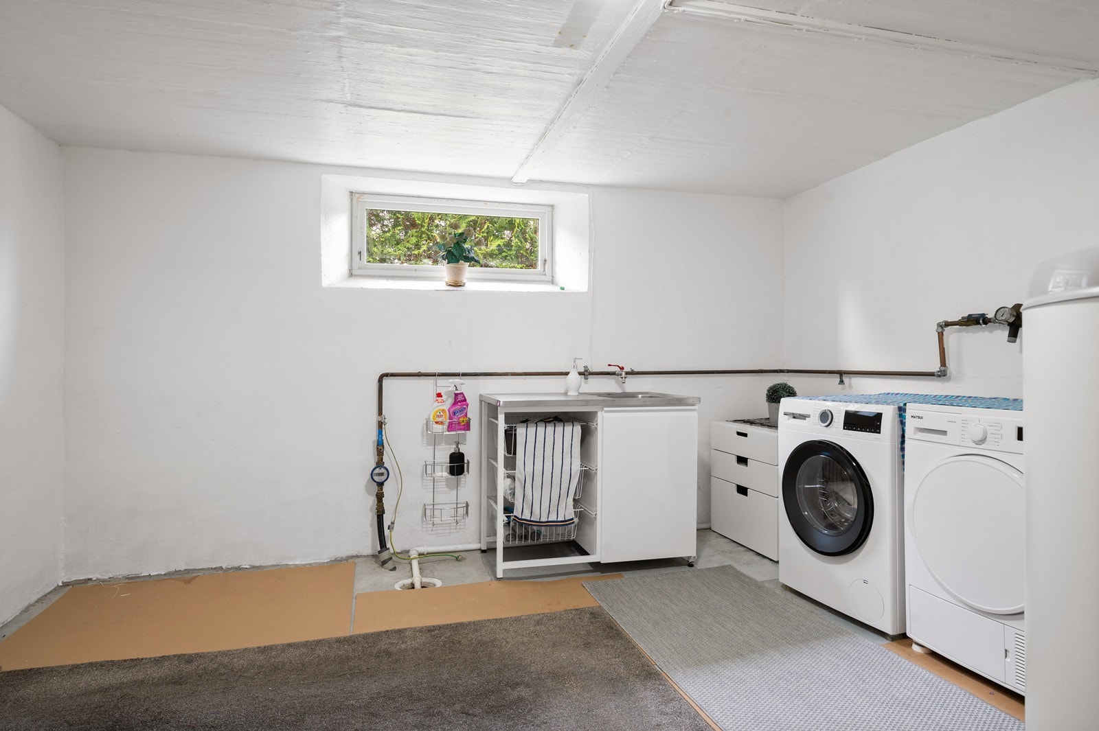 Stort og praktisk vaskerom i kjeller, med opplegg for vaskemaskin og tørketrommel. Her er også vannmåleren og varmtvannstanken plassert. Galleribilde