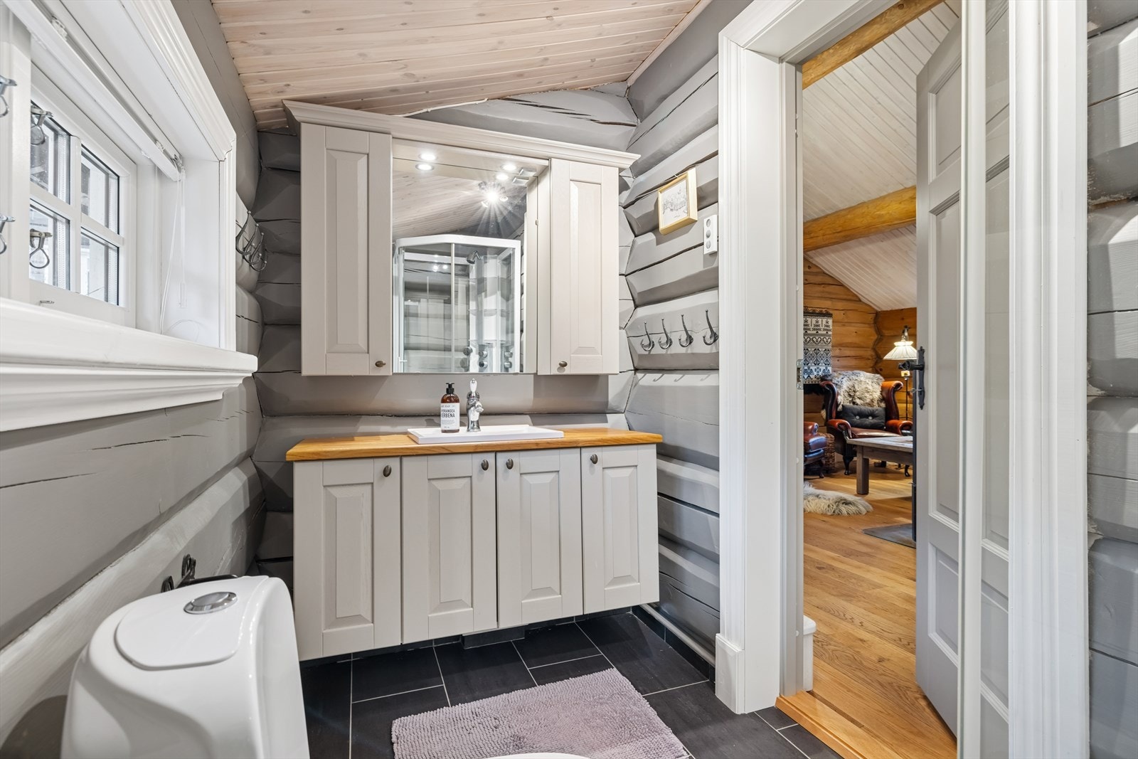 Lyst og praktisk bad med dusjkabinett, servant og toalett. Fliser på gulvet og moderne innredning gir et rent og innbydende preg. Elektrisk ventilasjon sørger for god luftkvalitet. Perfekt for både familie og gjester. Galleribilde