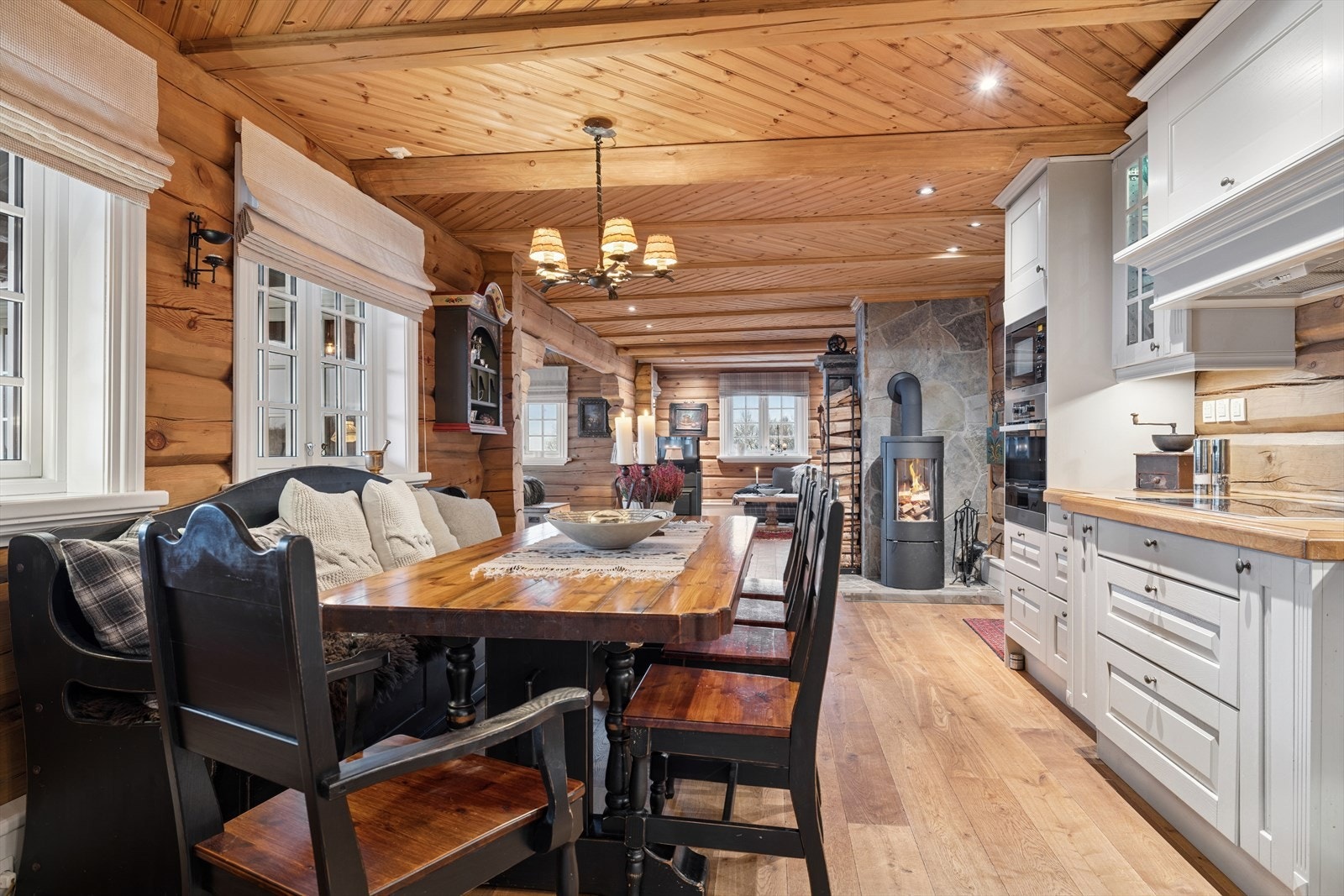 Kjøkkenet byr på rikelig plass til stort spisebord og mange stoler - perfekt for lange måltider og hyggelige sammenkomster. Her kan hele familien samles rundt bordet, med utsikt til peisovnen som også er vendt mot kjøkkenet Galleribilde