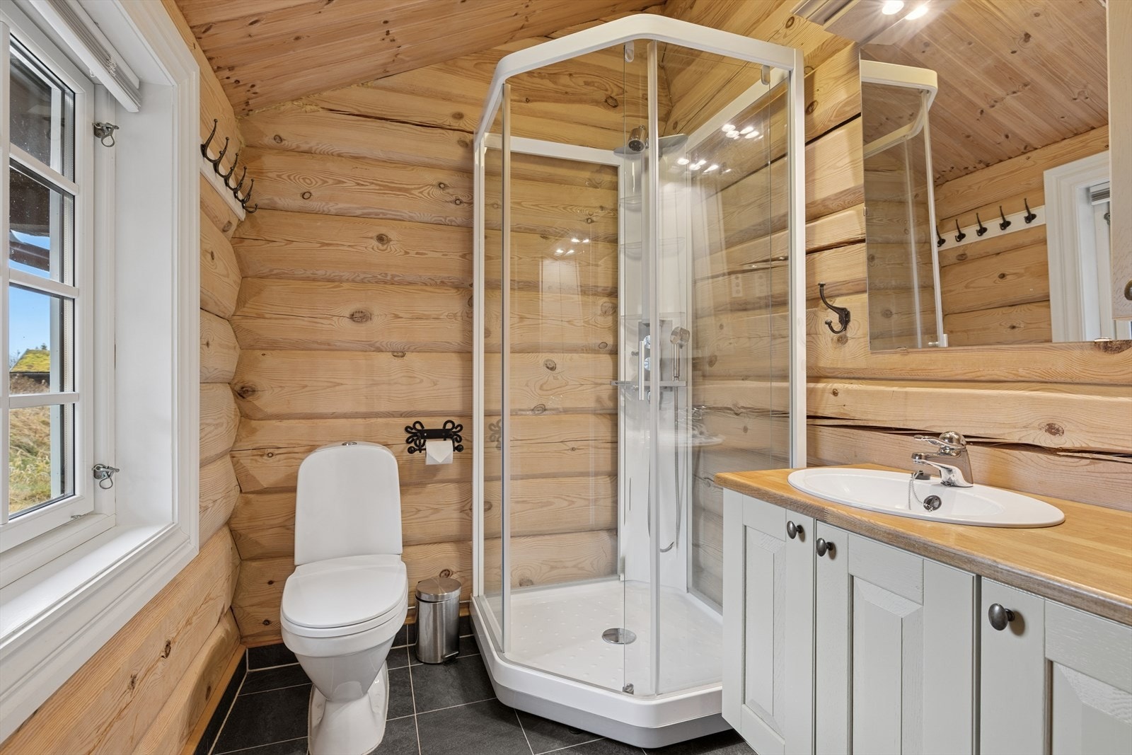 Lekkert bad med fliser på gulv, sokkelflis langs veggene, dusjkabinett, servant og toalett - alt du trenger for en komfortabel og praktisk hverdag på hytta. Galleribilde