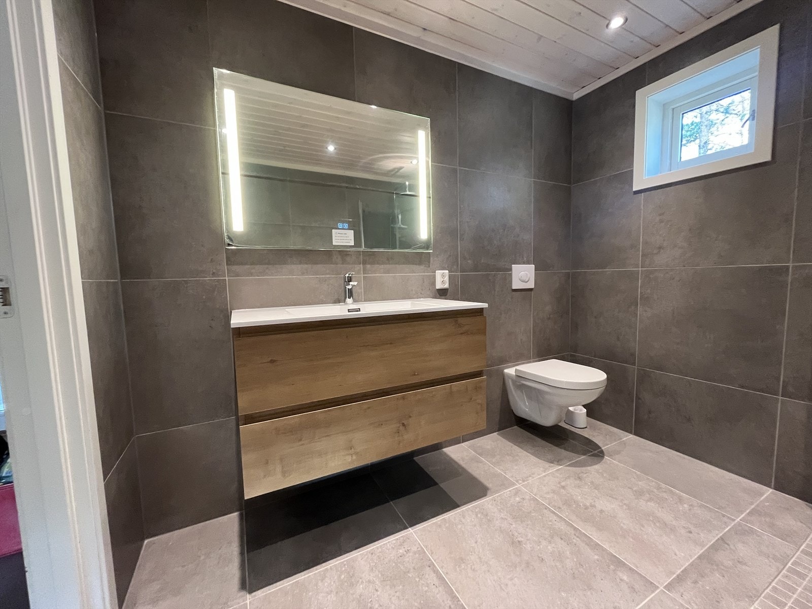 Badet har pene baderomsmøbler og vegghengt toalett Galleribilde