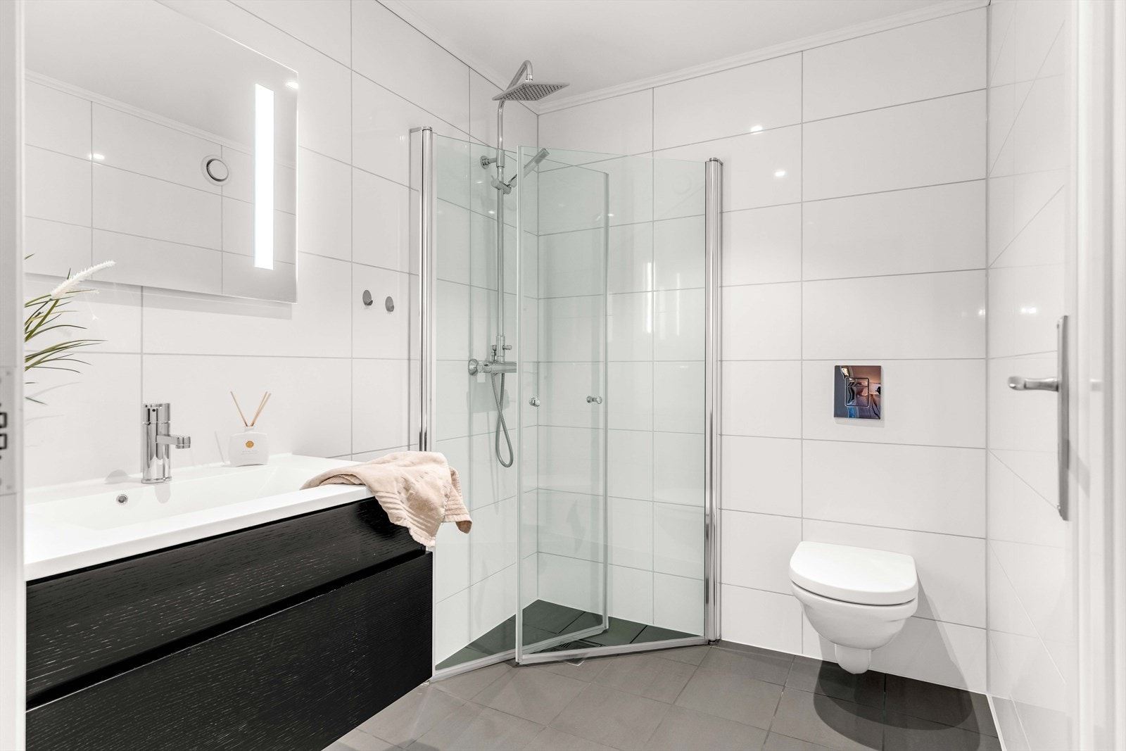 Det andre badet i etasjen har flislagte vegger og gulv med varmekabler. Innredningen består av en seksjon med glatte fronter, porselensvask med ettgreps servantbatteri og speil med integrert belysning. Badet har dusj og vegghengt toalett. Galleribilde