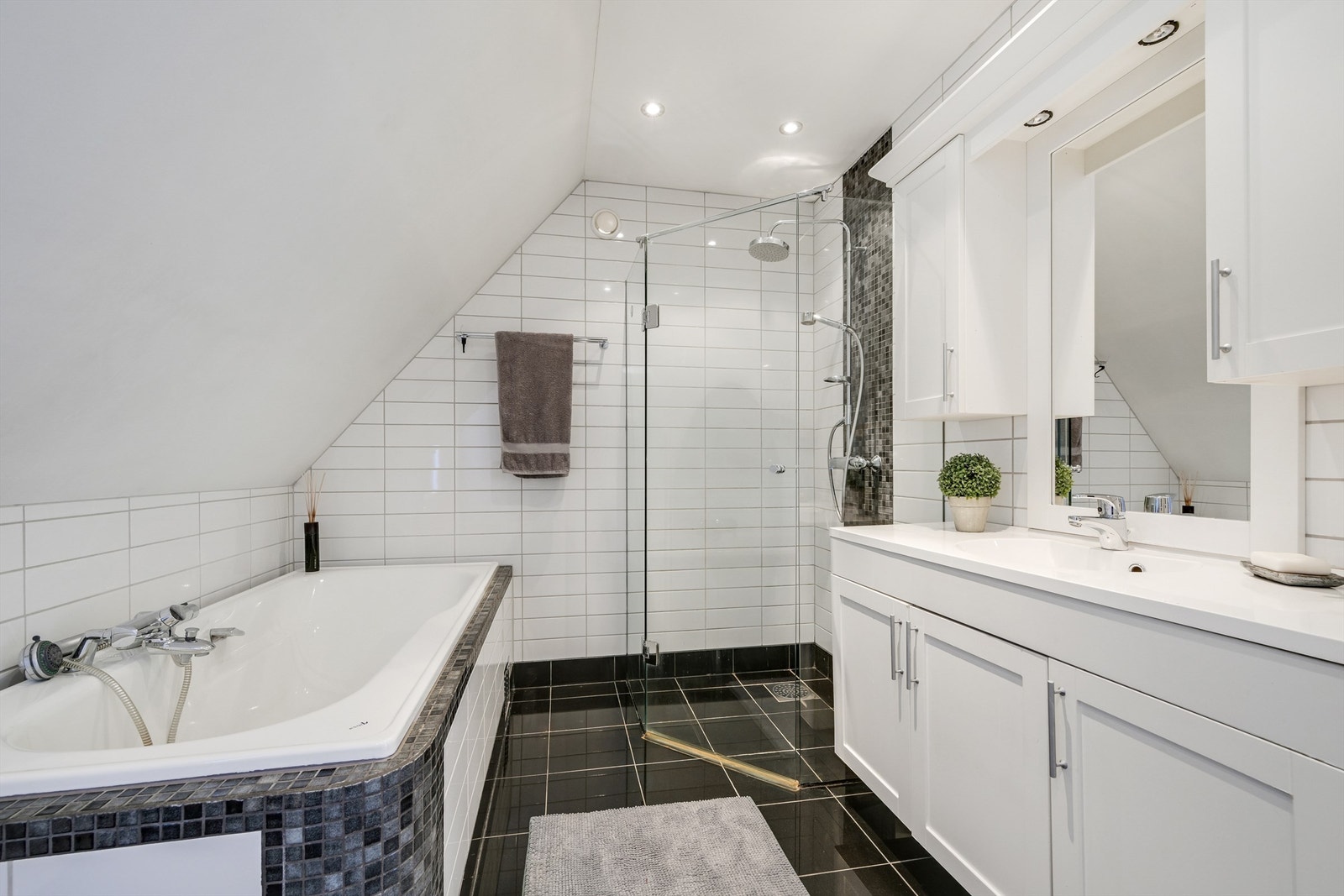 Badet er innredet med servant med underskap, innfliset badekar, dusjvegger og vegghengt toalett. Galleribilde