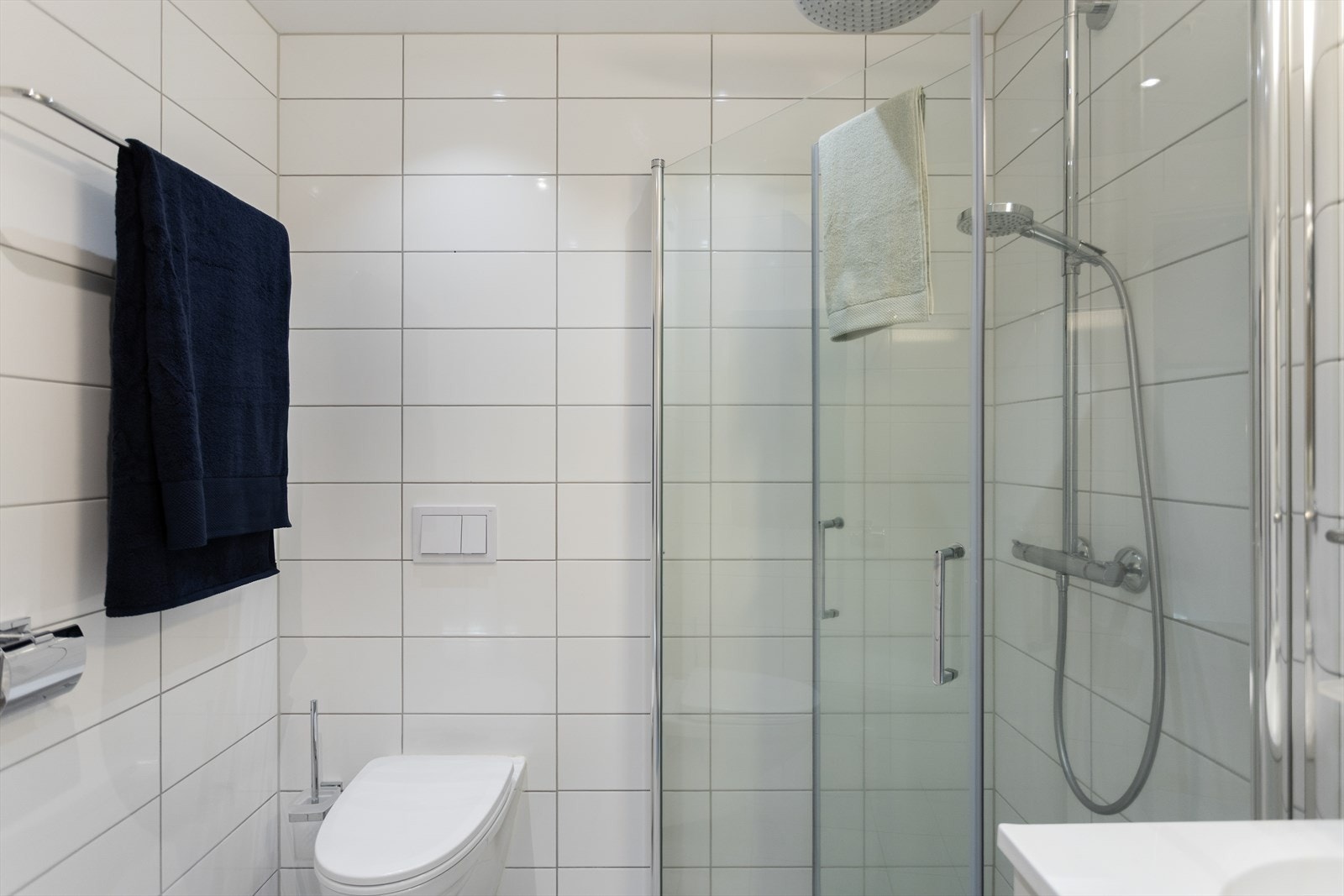 Det er utstyrt med dusjhjørne med innfellbare glassdører, servant med skap, speil med overlys og vegghengt toalett. Galleribilde