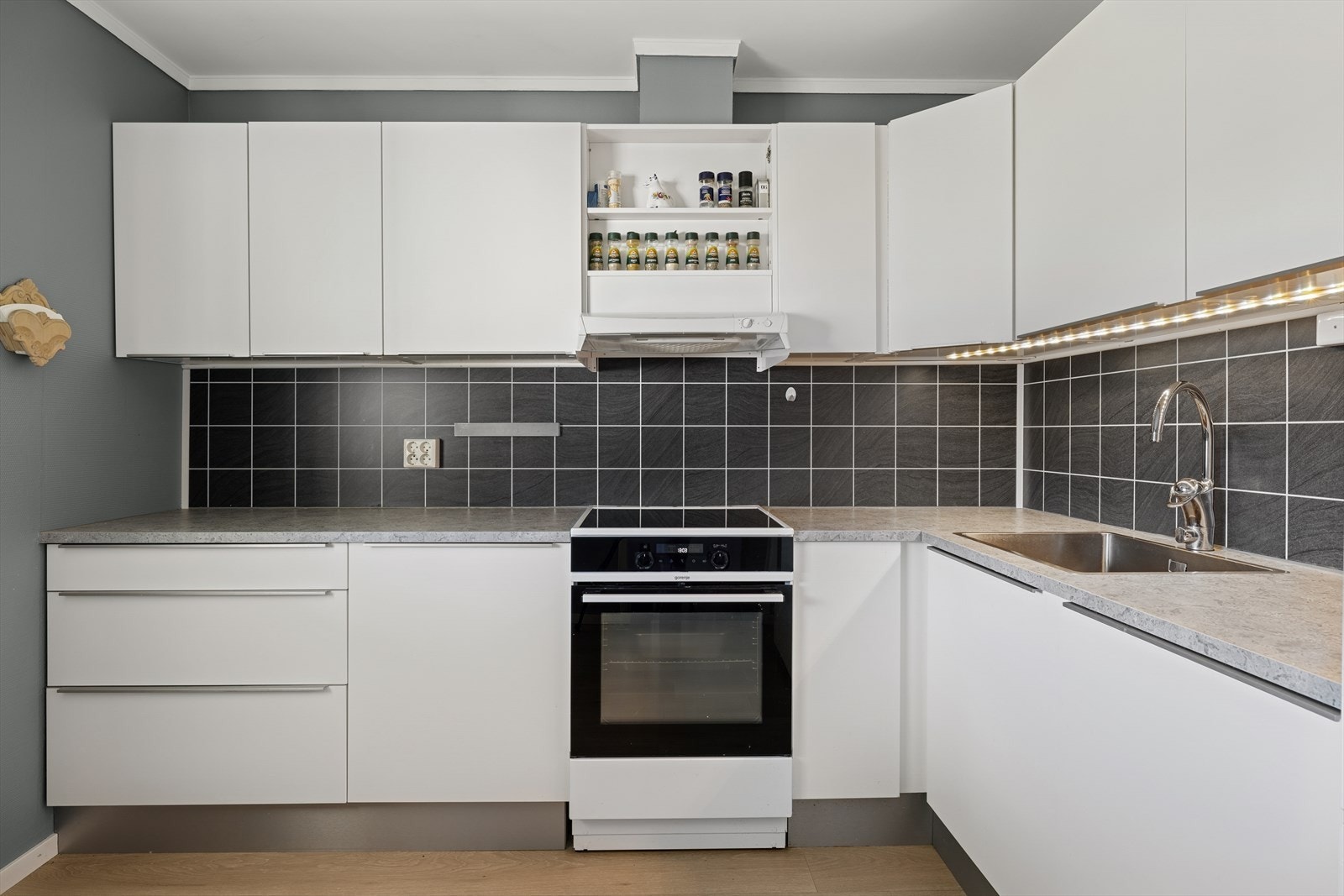 Kjøkkenet er videre utstyrt med blandebatteri i rustfritt stål, fliser på vegg bak platetopp/vask og det er kjøkkenventilator over stekesonen med mekanisk avtrekk. Galleribilde