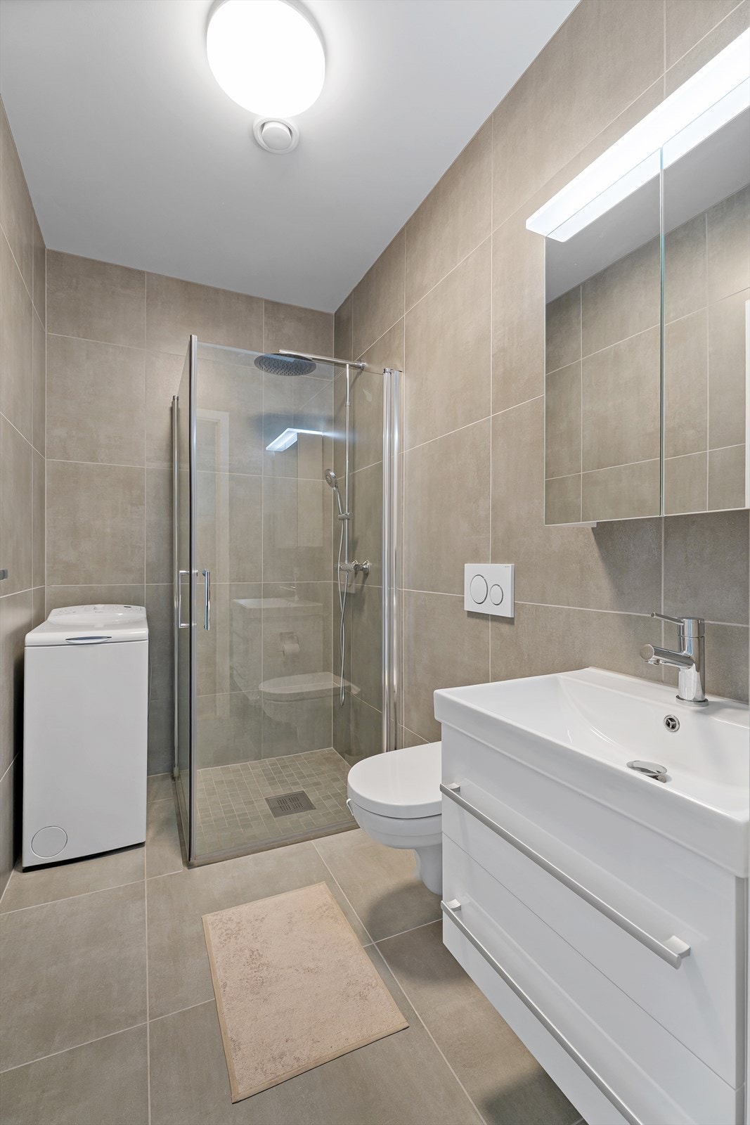 Flislagt bad m/varme i gulv. Servant med oppbevaring samt tilhørende speilskap. Opplegg til en mindre vaskemaskin. Galleribilde