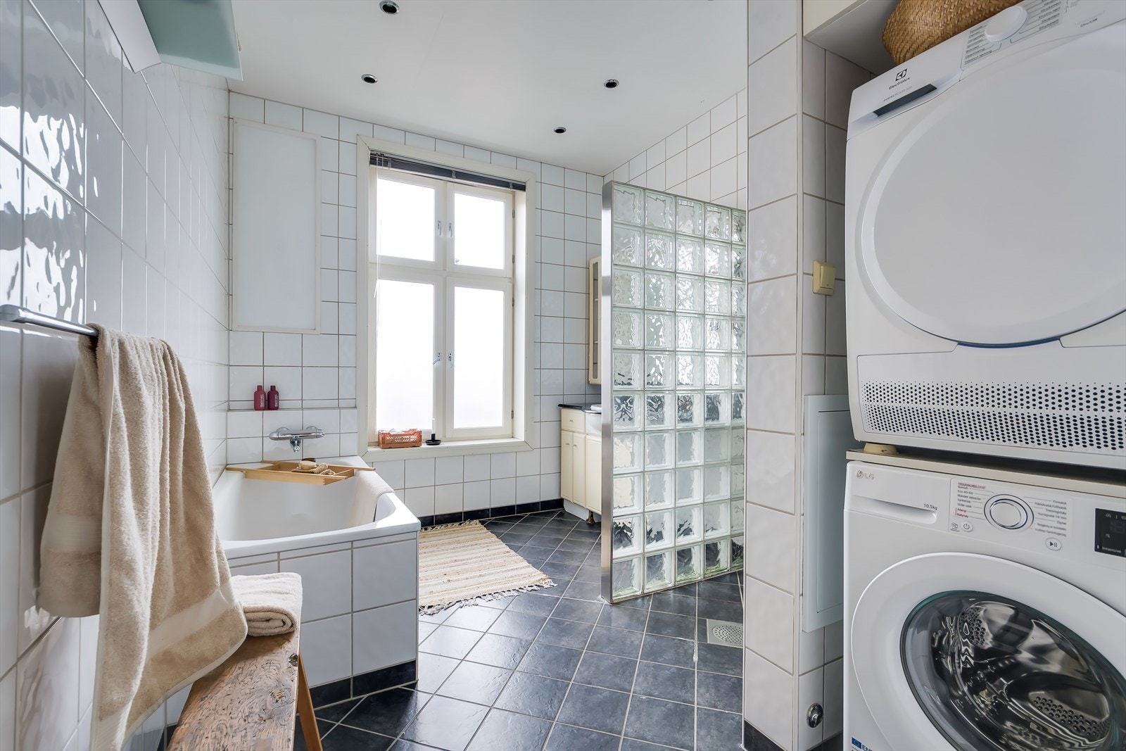 Stort, flislagt bad med badekar og dusjsone med glassbyggerstein og glassdør. Galleribilde