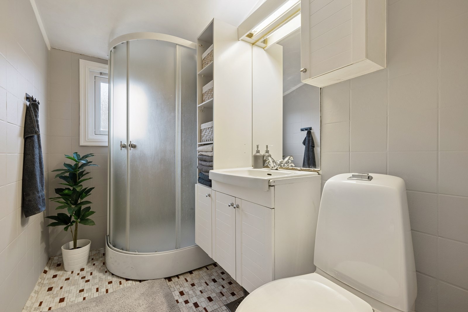 Gulvet har fliser uten gulvvarme, veggene har malte fliser, og himlingen består av en malt takflate. Rommet er innredet med en baderomsinnredning, toalett og dusjkabinett. Boligen har naturlig ventilasjon. Galleribilde