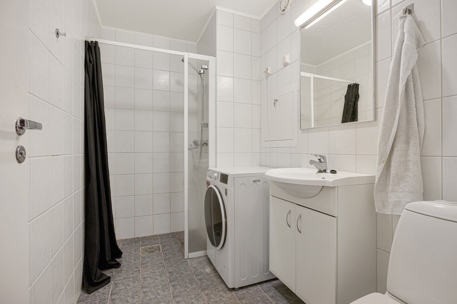 Badet i leiligheten fremstår som velholdt og pent, med hvite fliser på veggene og grå fliser på gulv med gulvvarme. Galleribilde