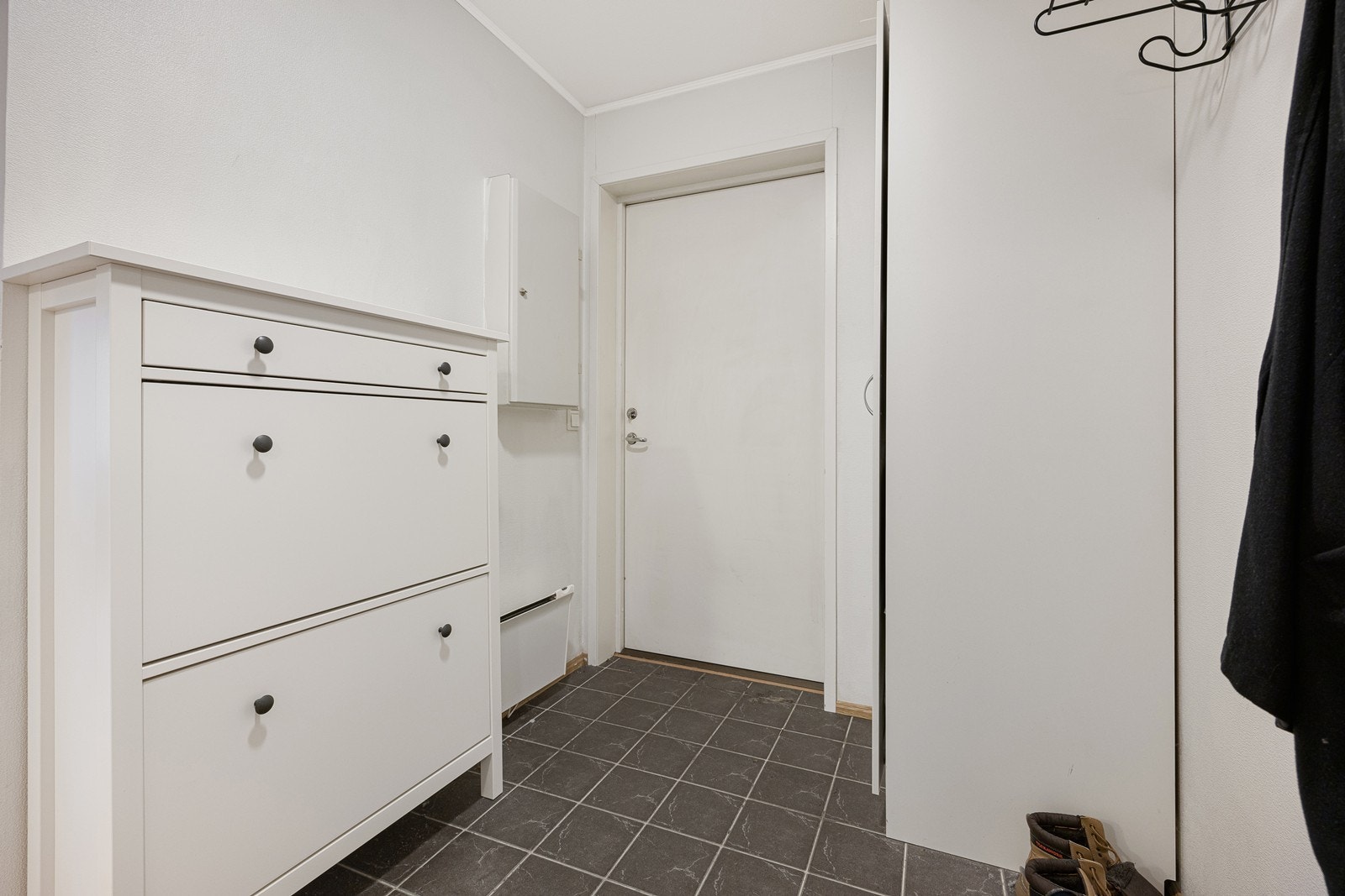 Entreen er stilren og pen, med hvitmalte vegger mot grått, flislagt gulv. Galleribilde